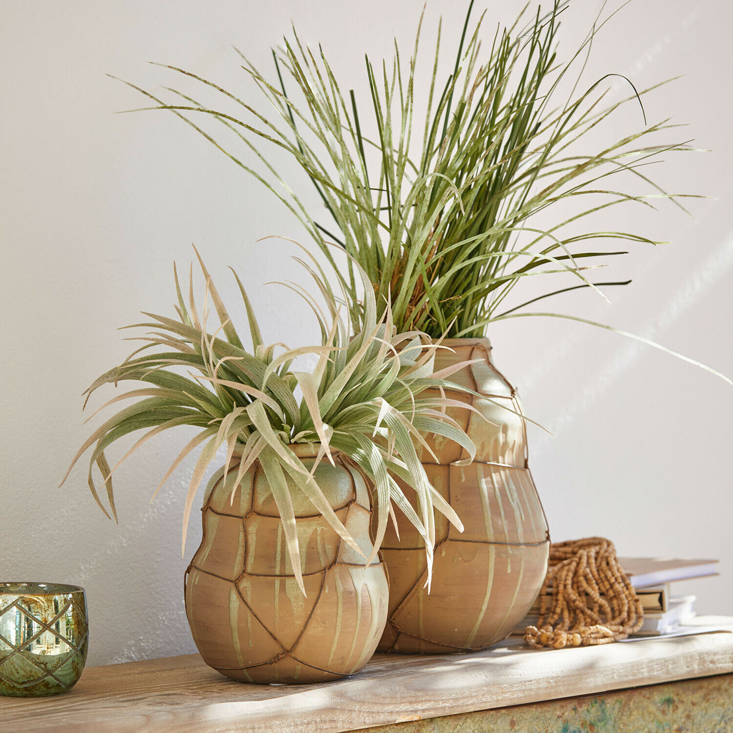 Dwie ceramiczne wazony w kolorze beżowym z zielonymi roślinami dekoracyjnymi na drewnianym stole