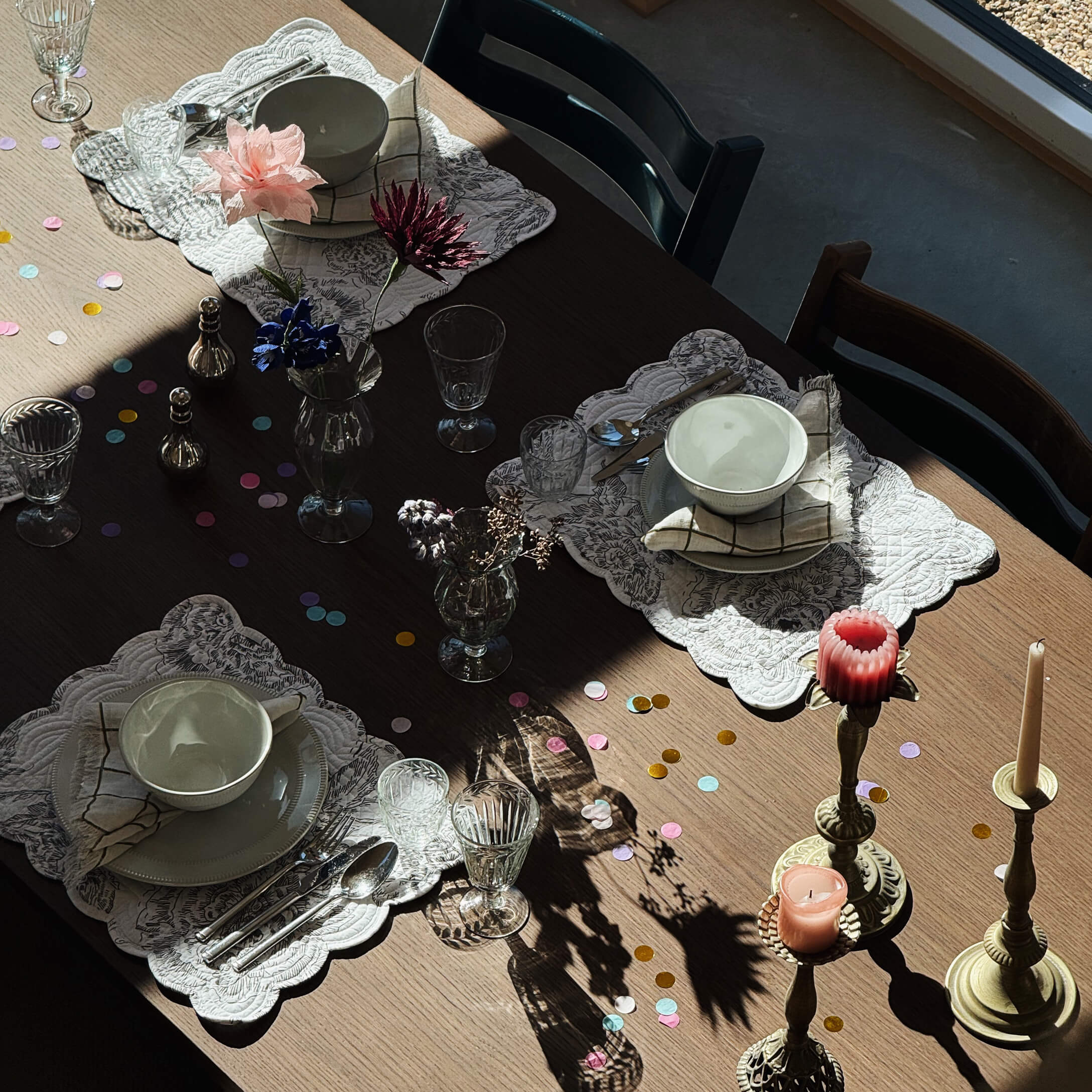 Drewniany stół z białymi ceramicznymi miskami, szklankami i świecami na mosiężnych świecznikach