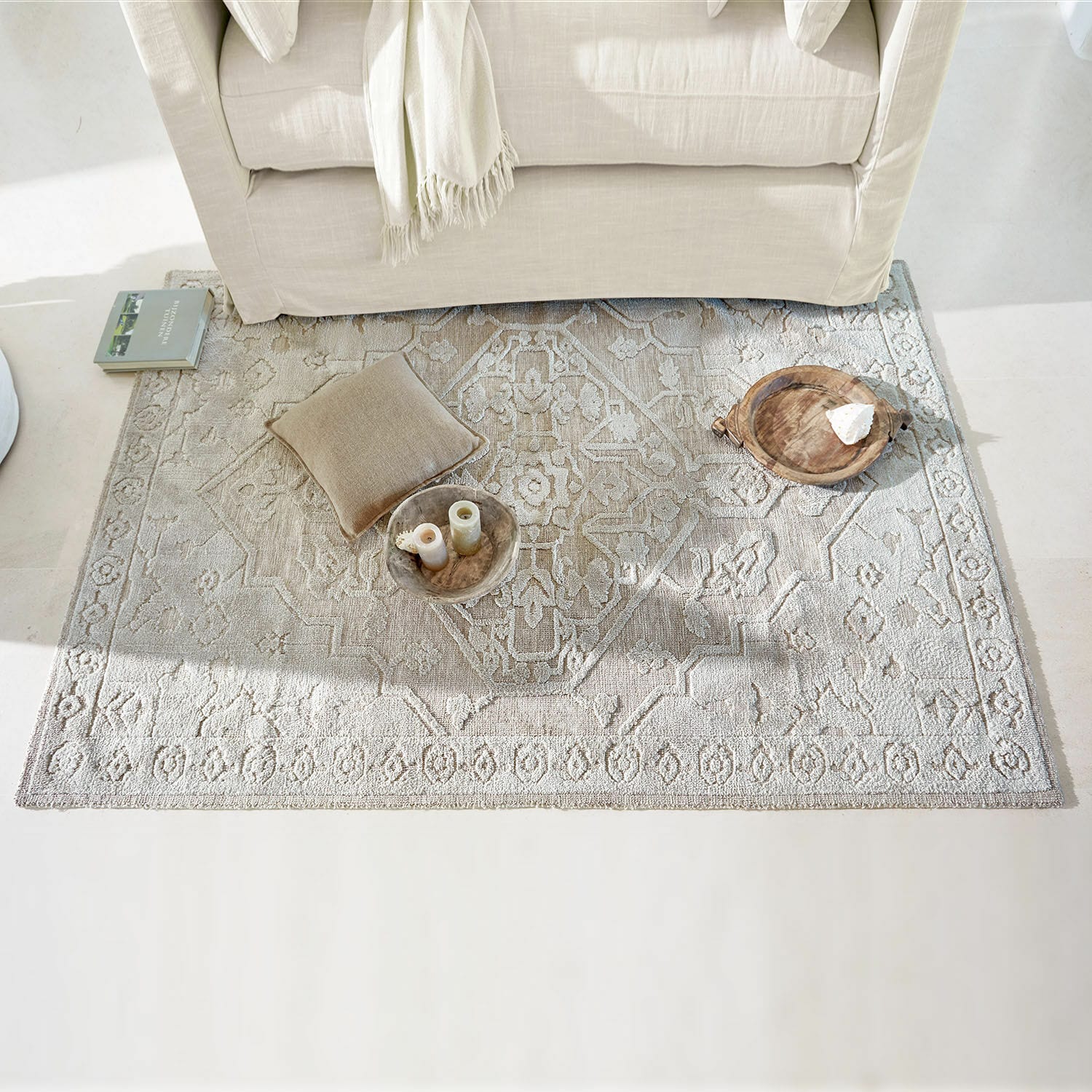 Dywan Armidale Beżowy dywan z delikatnym wzorem pod jasną sofą, dekoracje i poduszka na podłodze