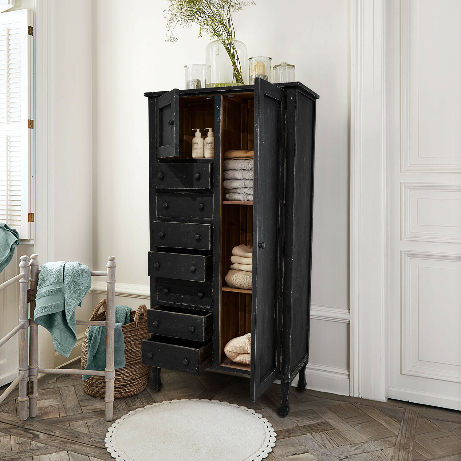 Czarna drewniana szafka z szufladami i półkami, przechowująca ręczniki i kosmetyki w łazience