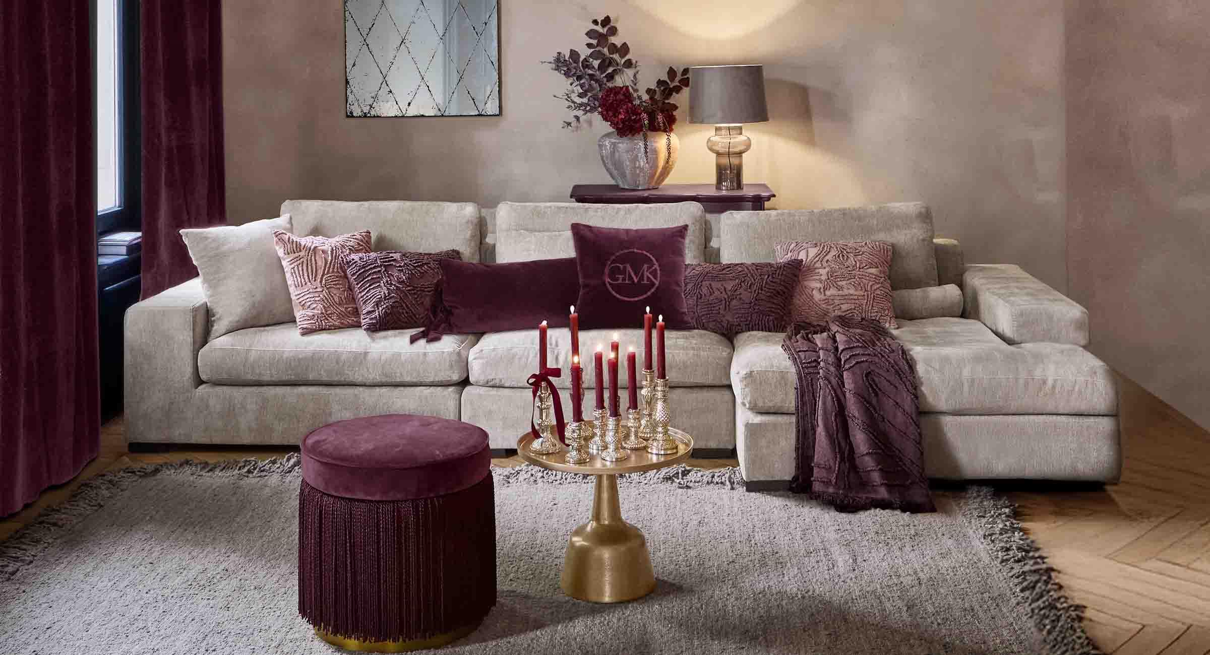 Beżowa sofa z miękkimi poduszkami i bordowymi dodatkami w eleganckim salonie z lampą i lustrem
