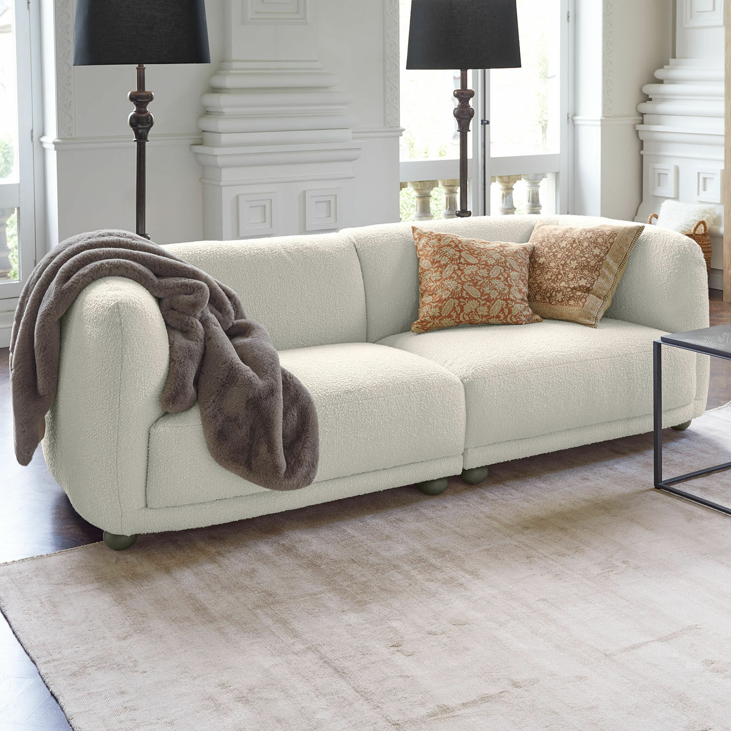 Sofa Scintillique Nowoczesna sofa w kolorze kremowym z miękkim materiałem i dekoracyjnymi poduszkami w salonie