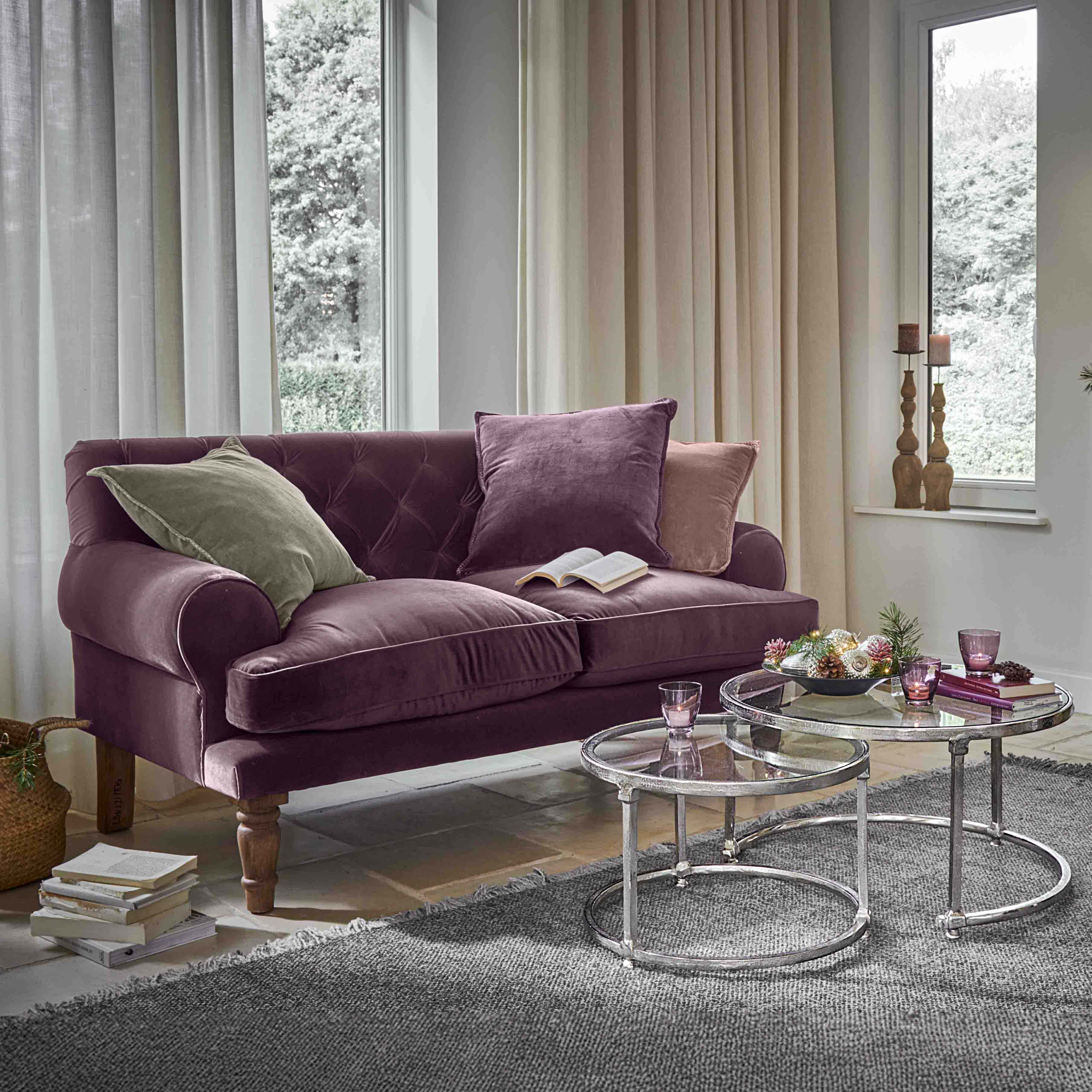Fioletowa aksamitna sofa z poduszkami i szklanymi stolikami kawowymi w jasnym salonie