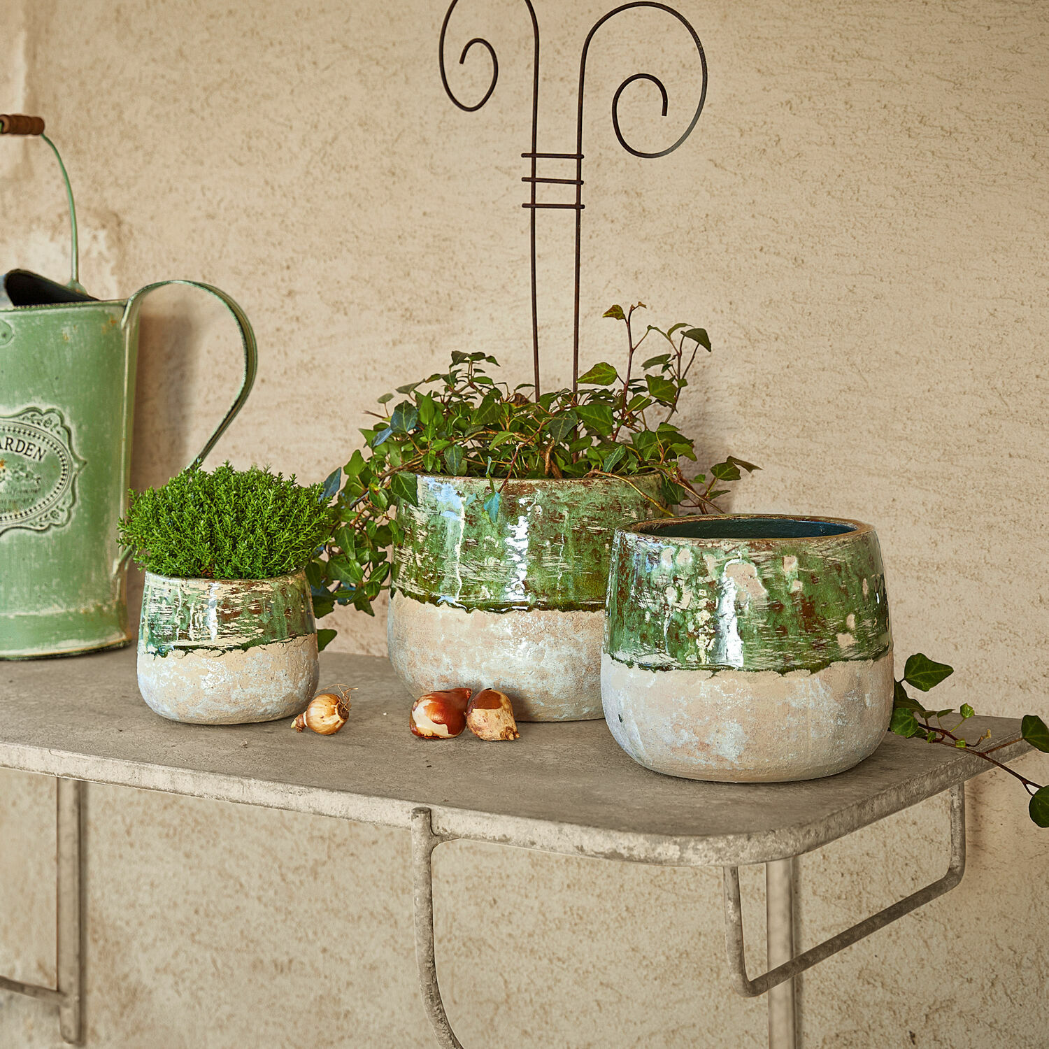 Osłonka doniczki, zestaw 3 szt. Reefton Zestaw trzech ceramicznych donic w zielono-beżowym kolorze na metalowej półce do dekoracji ogrodu