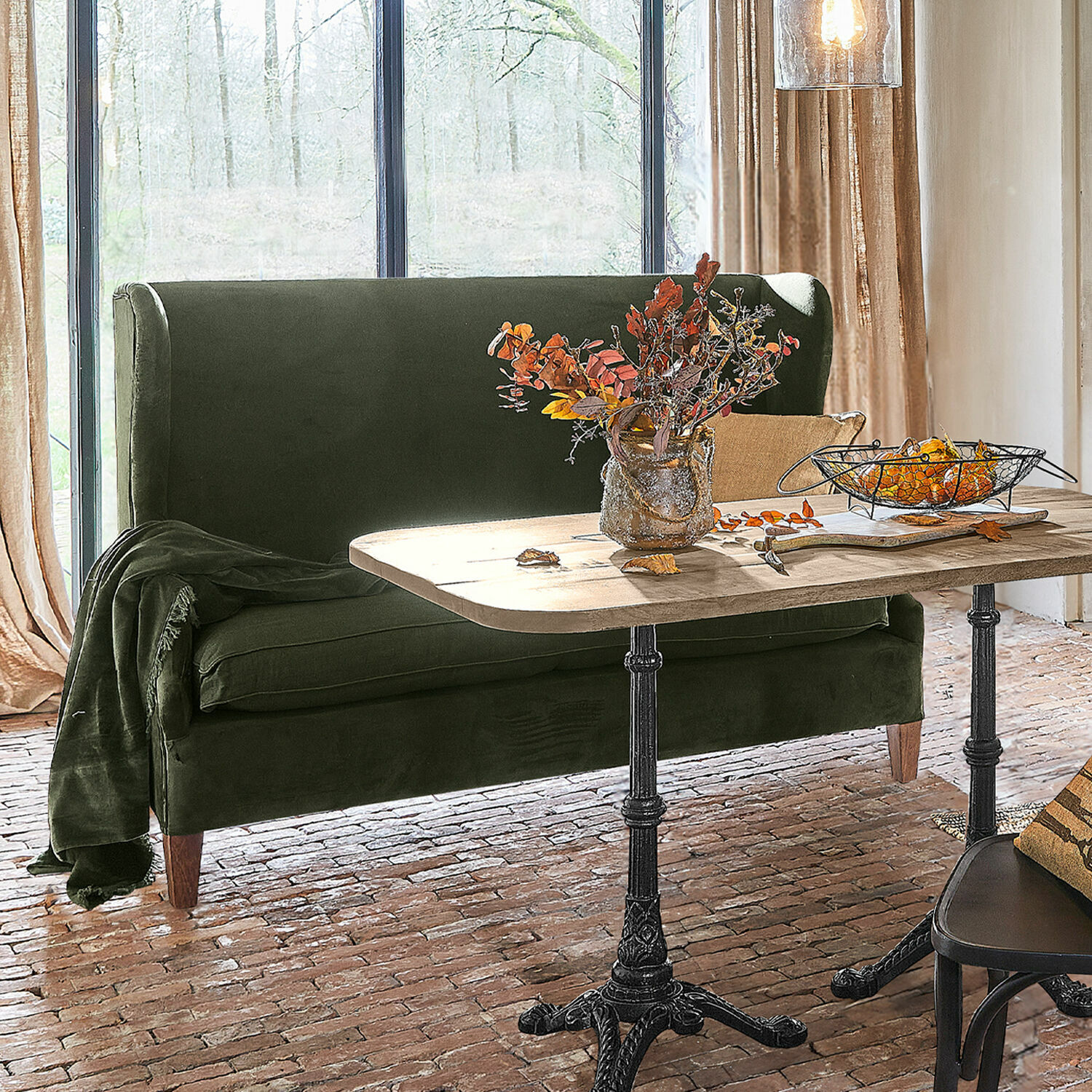 Sofa Ombra Zielona aksamitna sofa przy drewnianym stole z metalowymi nogami w jasnym salonie z ceglaną podłogą
