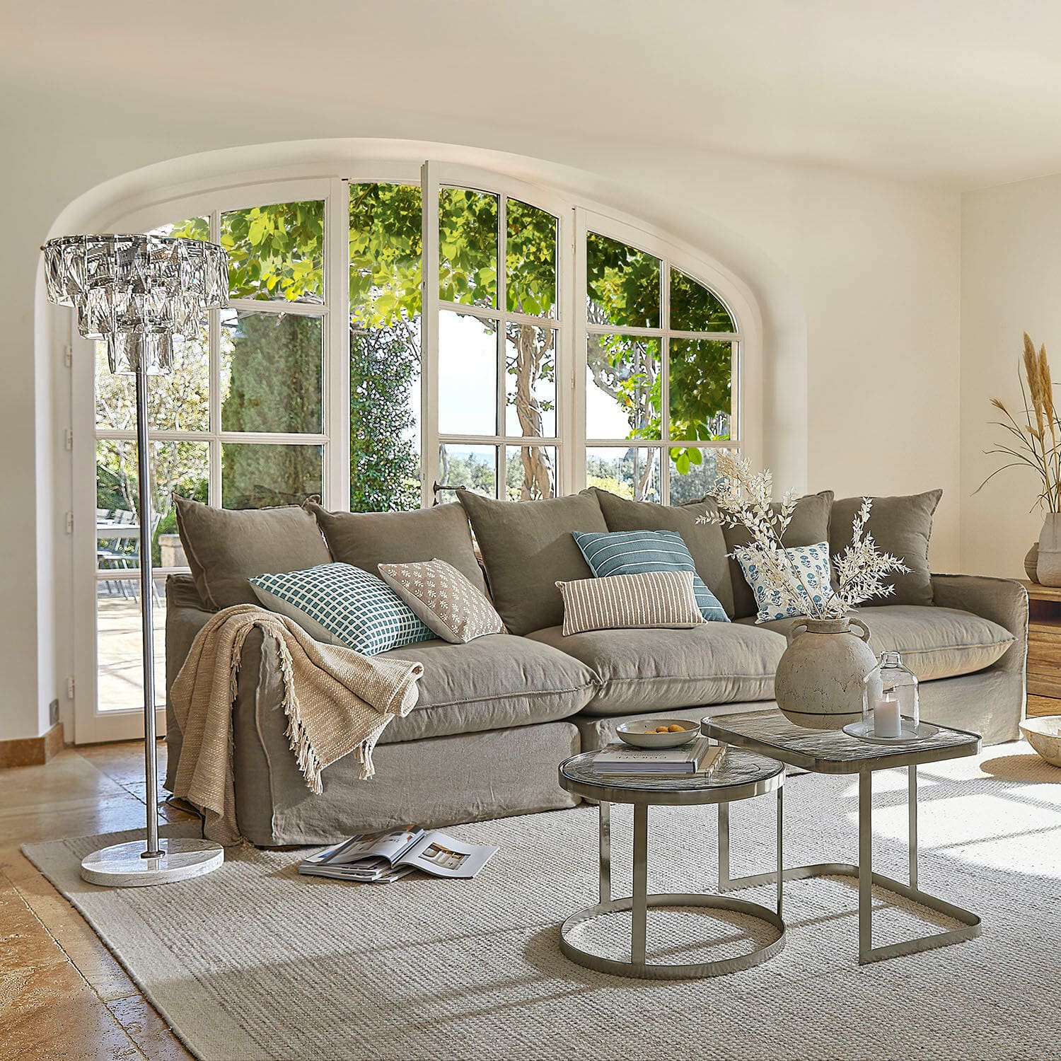 Sofa Finchingfield Przytulna szara sofa z poduszkami i stolikami kawowymi w jasnym salonie z dużymi oknami