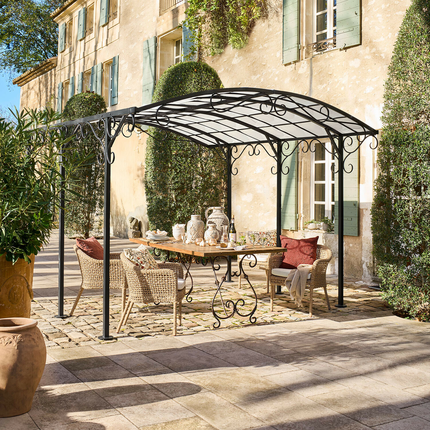 Pergola Delbridge Altana ogrodowa z czarnego metalu z ozdobnymi zawijasami nad drewnianym stołem i wiklinowymi krzesłami