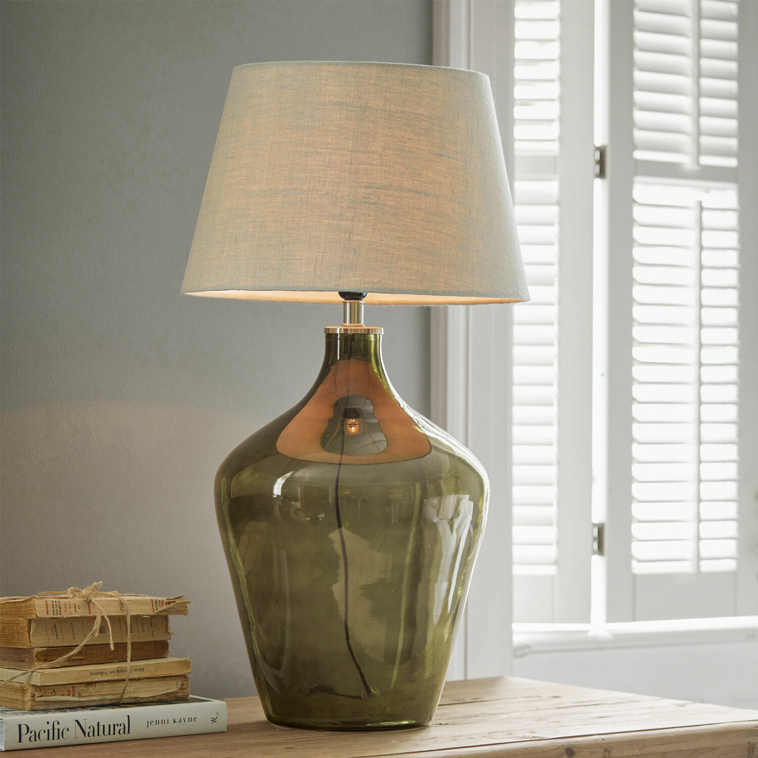 Lampa stołowa Morazan Lampka stołowa z zielonego szkła z beżowym abażurem na drewnianym stole z książkami