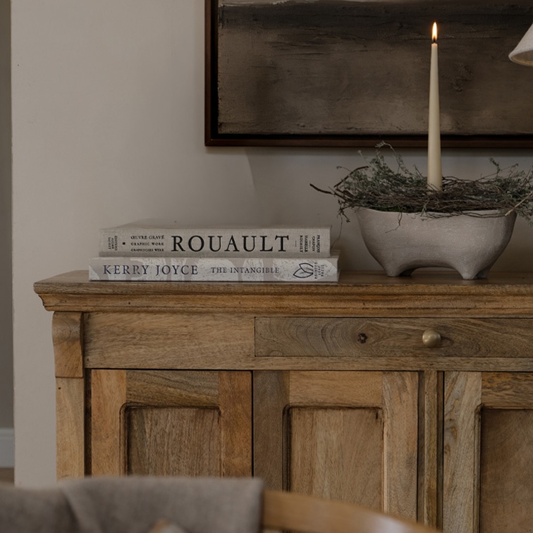 Drewniana komoda z dwoma książkami i świecą w ceramicznej misie na dekoracyjnym stole w salonie