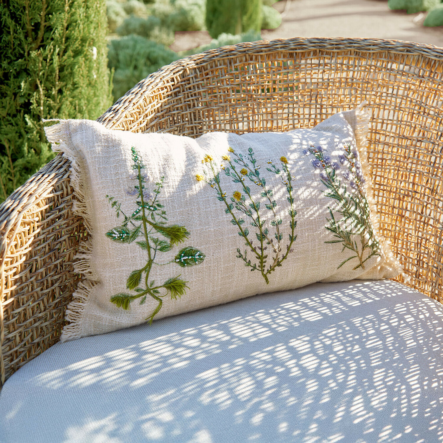 Beżowa lniana poduszka z haftem roślinnym na wiklinowym fotelu, dekoracja ogrodowa