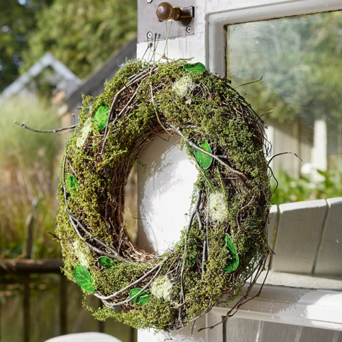 Naturalny wieniec z mchu i gałązek z zielonymi liśćmi, dekoracja drzwi na zewnątrz