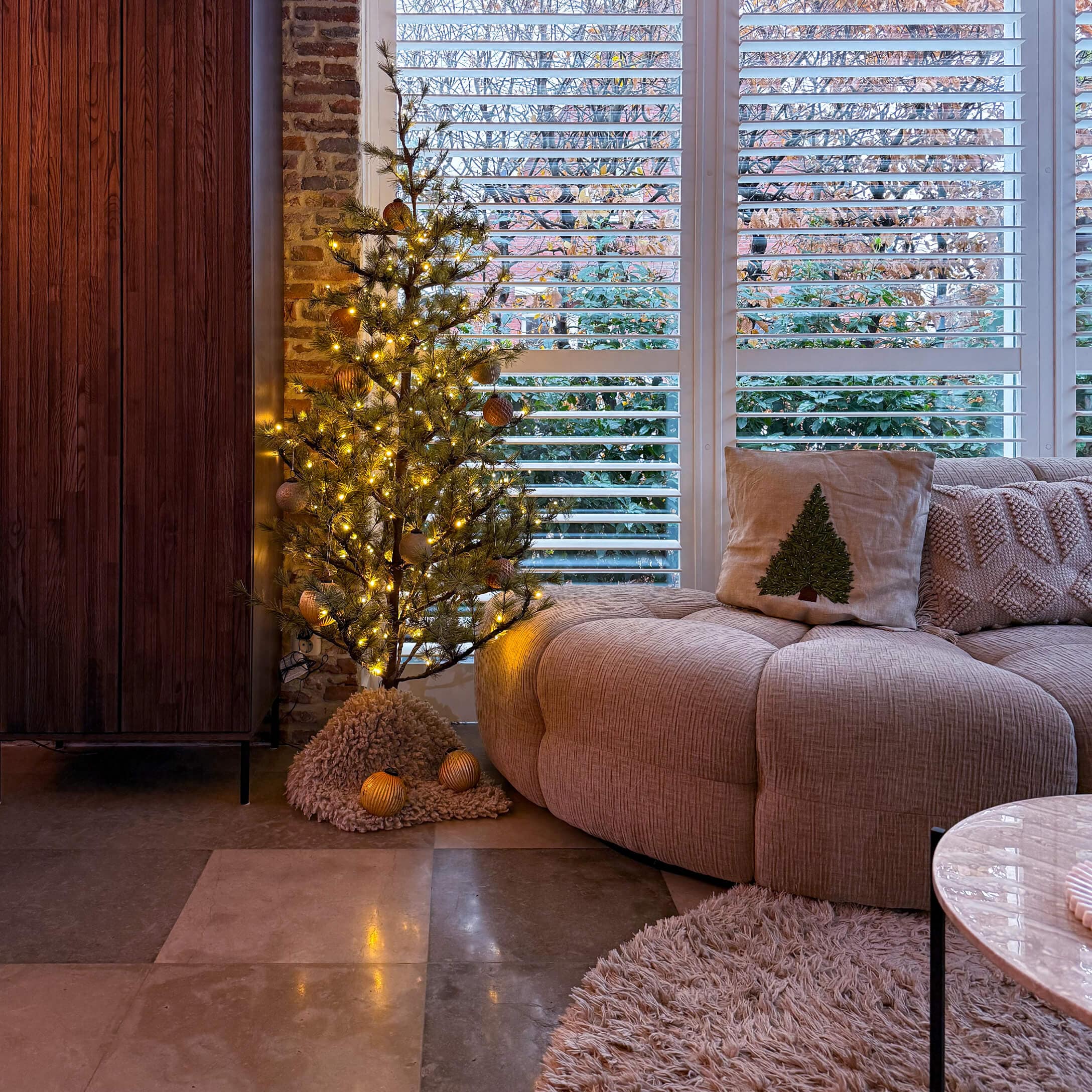 Przytulny salon z beżową sofą, poduszką z choinką i oświetloną dekoracyjną choinką LED