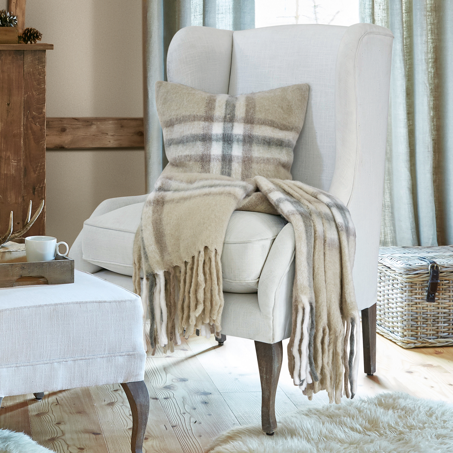 Beżowa wełniana narzuta i poduszka w kratę na kremowym fotelu w przytulnym salonie