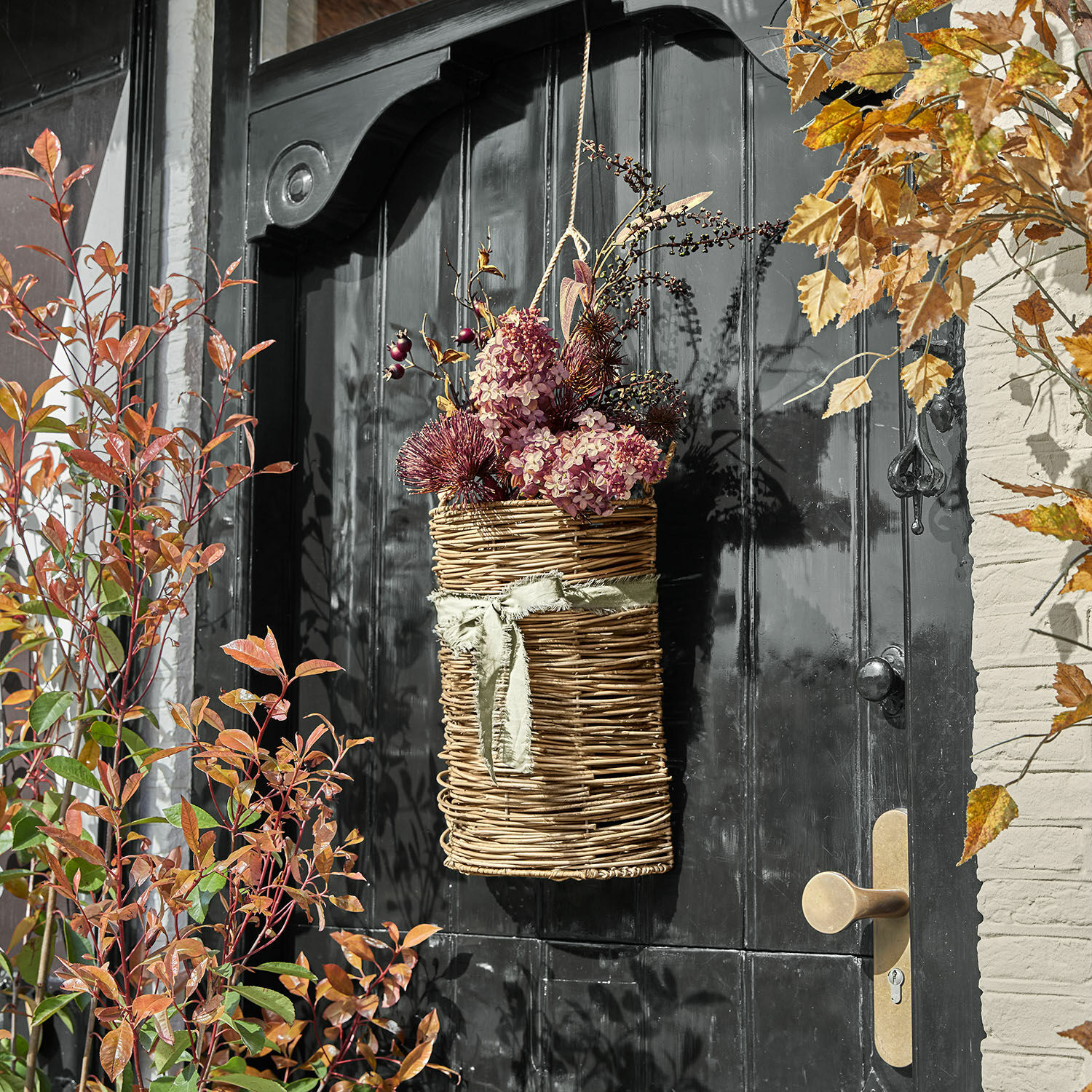 Wiszący kosz z wikliny z dekoracją z suszonych kwiatów na czarnych drzwiach wejściowych