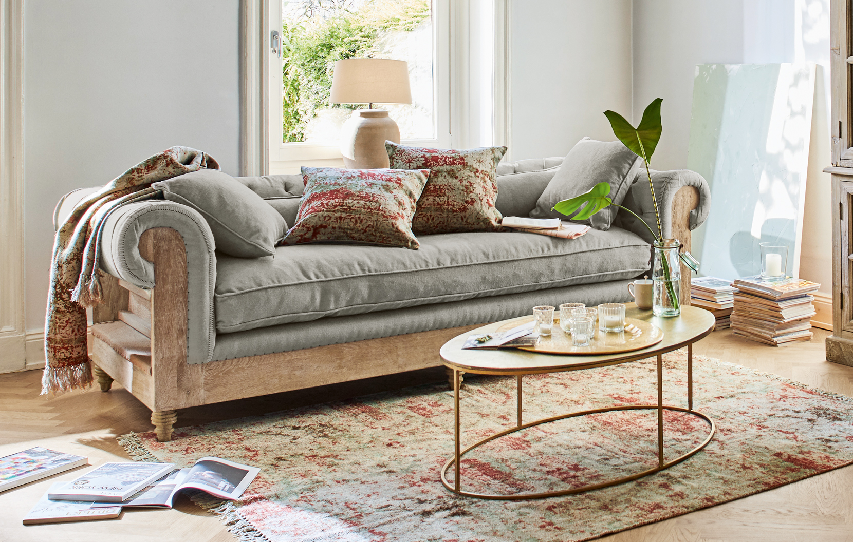 Szara sofa z drewnianą ramą i orientalnym dywanem w jasnym salonie z dekoracyjnymi poduszkami