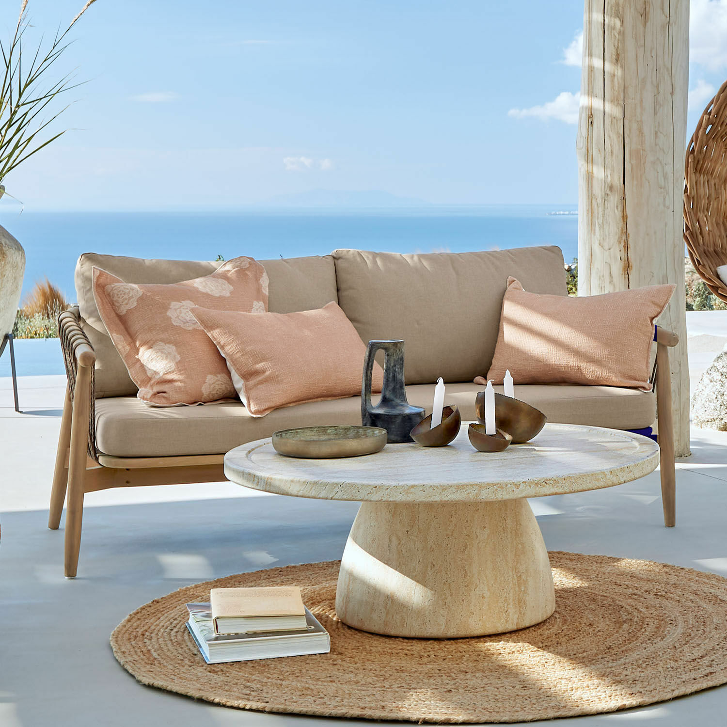 Sofa FSC®-100% Thornwick Beżowa sofa z poduszkami i okrągły stół z kamienia na tarasie z widokiem na morze