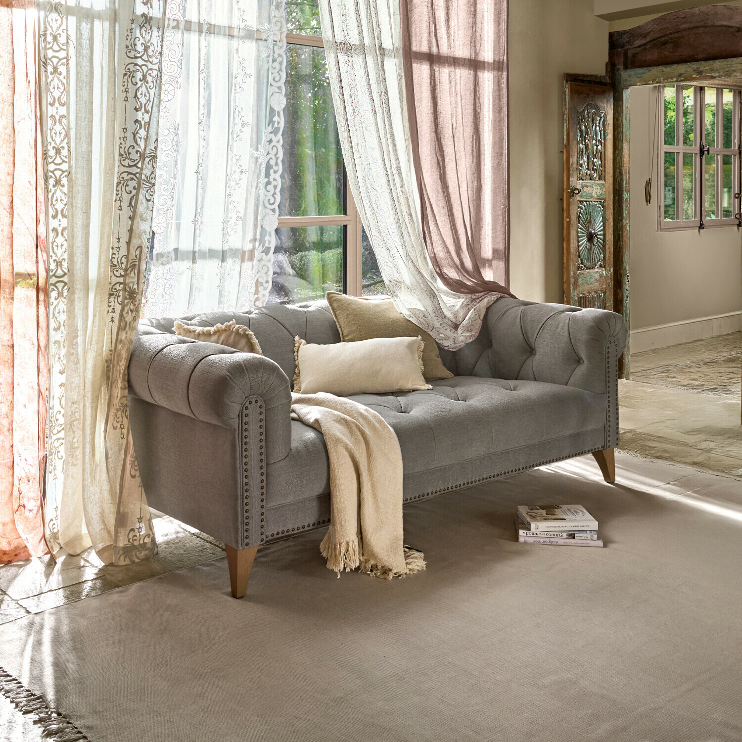 Sofa Sanbornville Szara tapicerowana sofa z drewnianymi nogami i beżowymi poduszkami w jasnym salonie z zasłonami