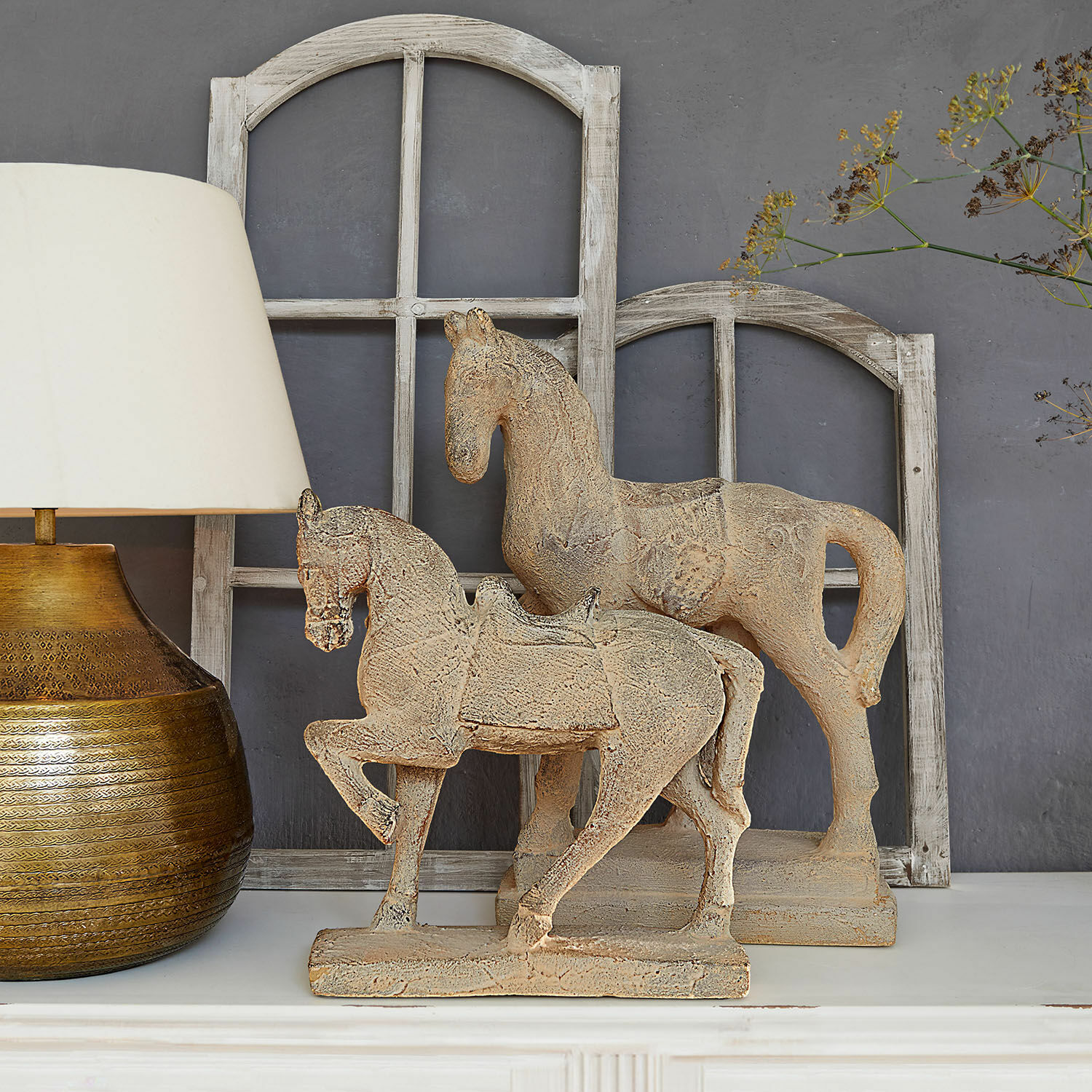 Dekoracyjny koń, zestaw 2 szt. Mirandel Dekoracyjne figury koni z beżowego kamienia na białej półce z lampą i drewnianymi ramami okiennymi