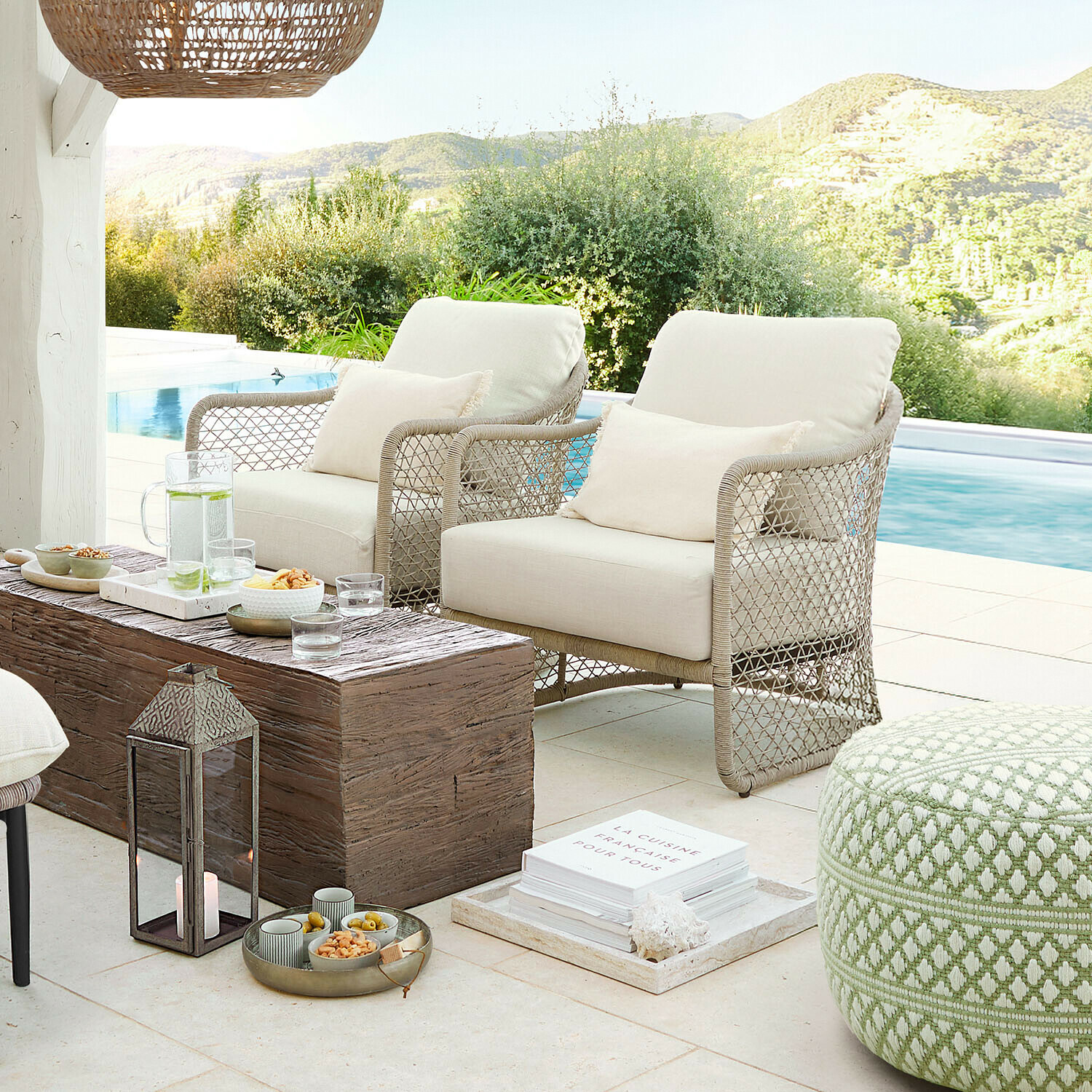 Dwa beżowe fotele z plecionego materiału na tarasie przy basenie z drewnianym stolikiem i zielonym pufem
