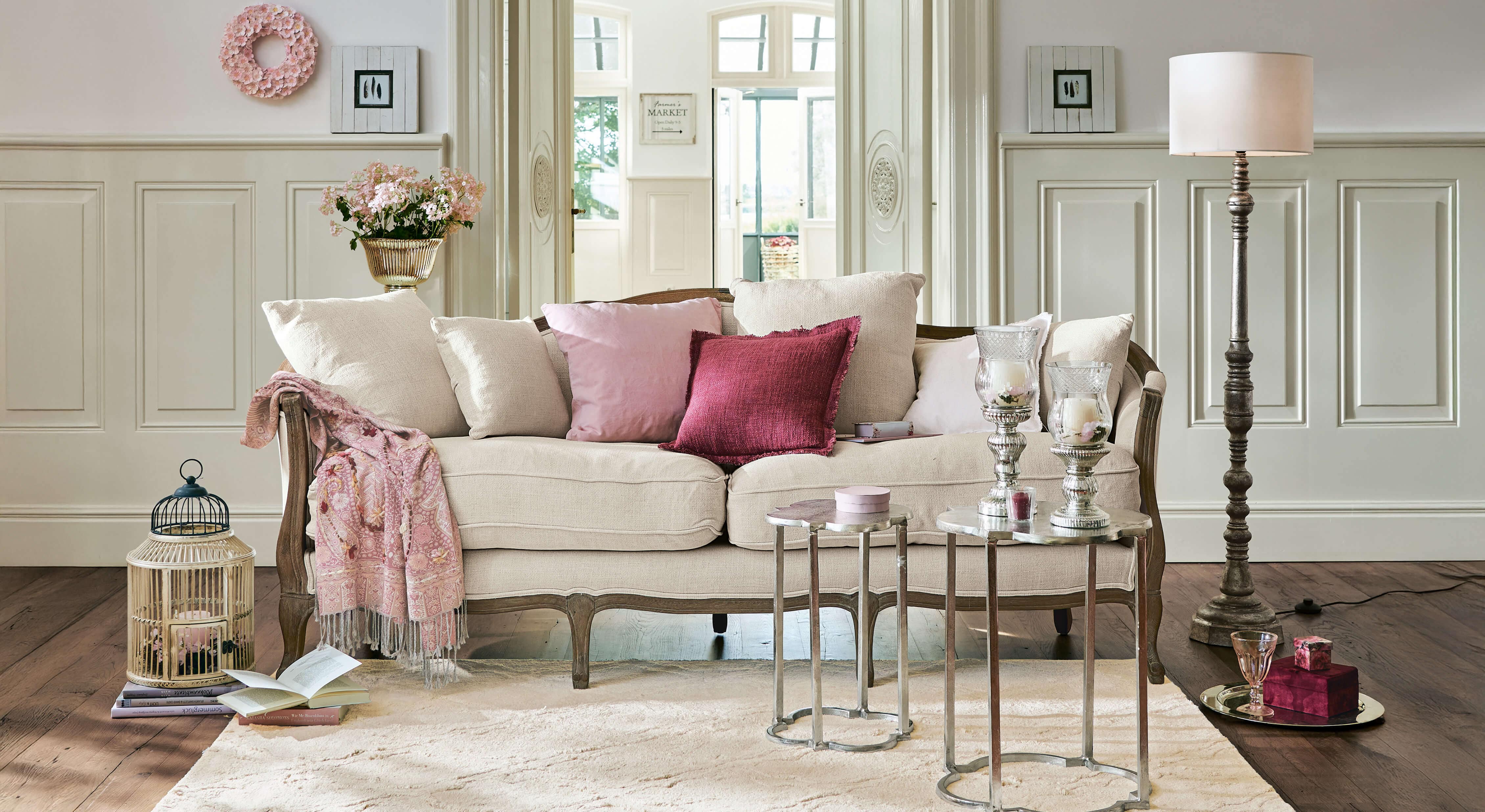 Beżowa sofa z drewnianą ramą i różowymi poduszkami w eleganckim salonie z dekoracjami