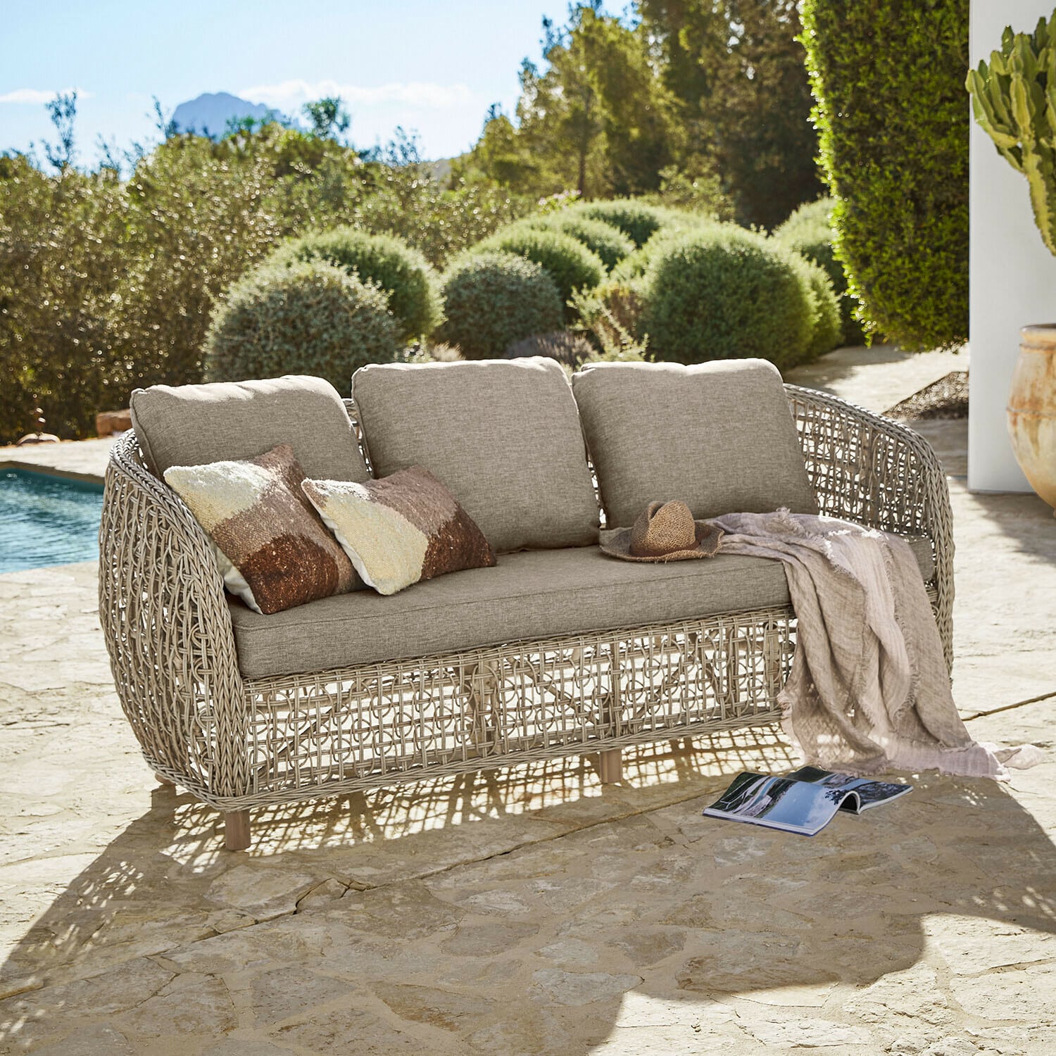 Sofa ogrodowe z beżową poduszką i plecionym stelażem z rattanu na kamiennym tarasie przy basenie