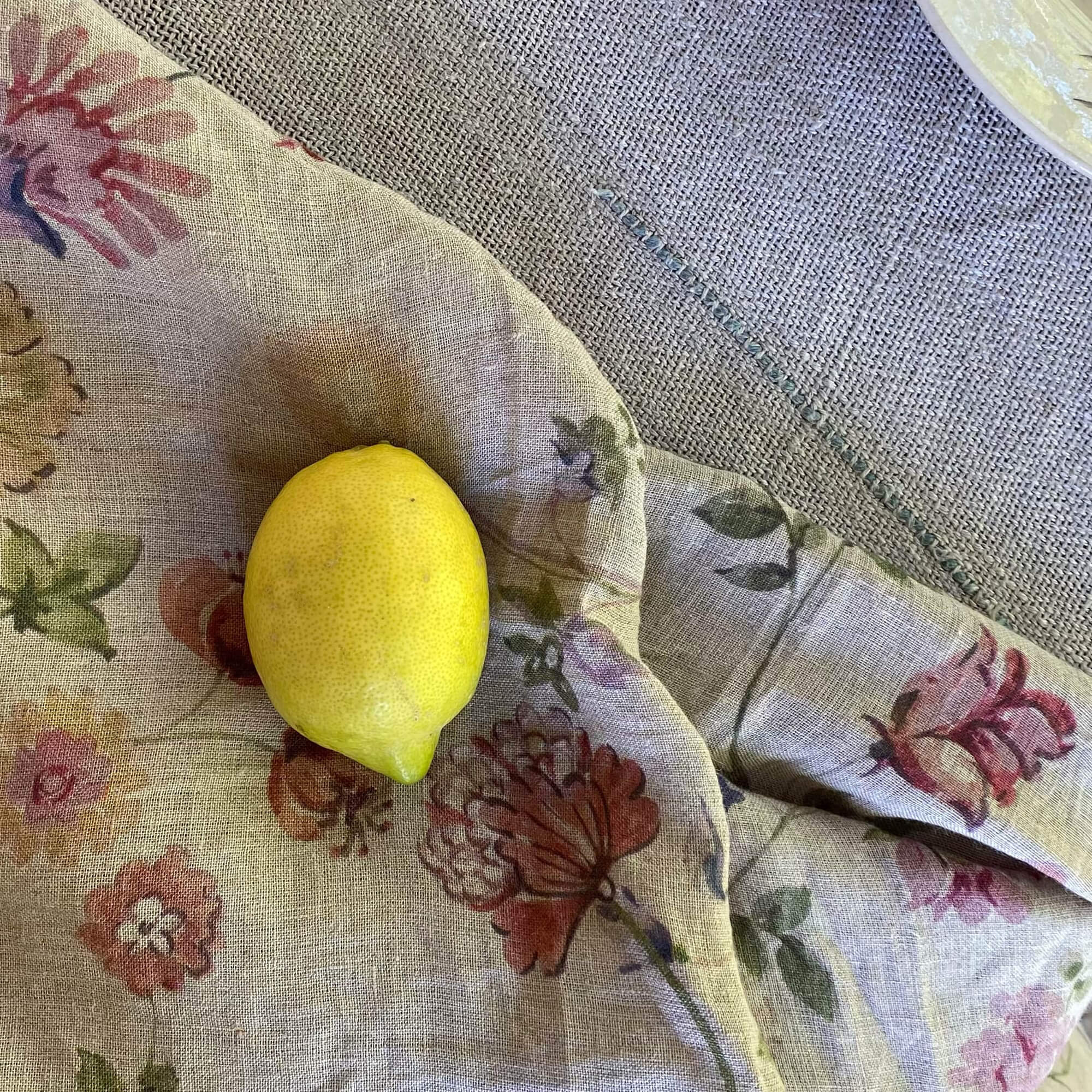 Lniany obrus w kwiatowy wzór w pastelowych kolorach z żółtą cytryną na środku, dekoracja stołu