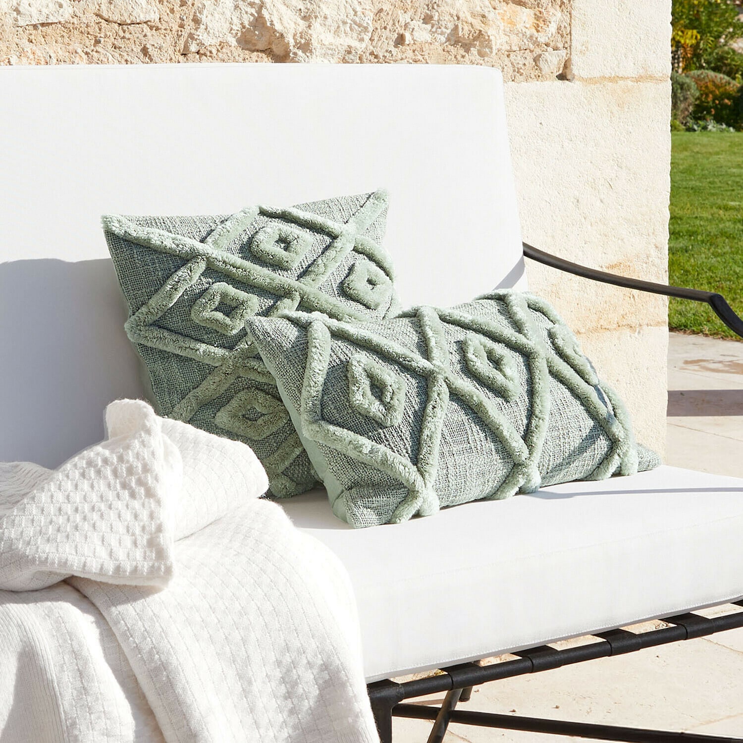 Miętowe dekoracyjne poduszki z geometrycznym wzorem na białej sofie z kocem, tekstylia do salonu