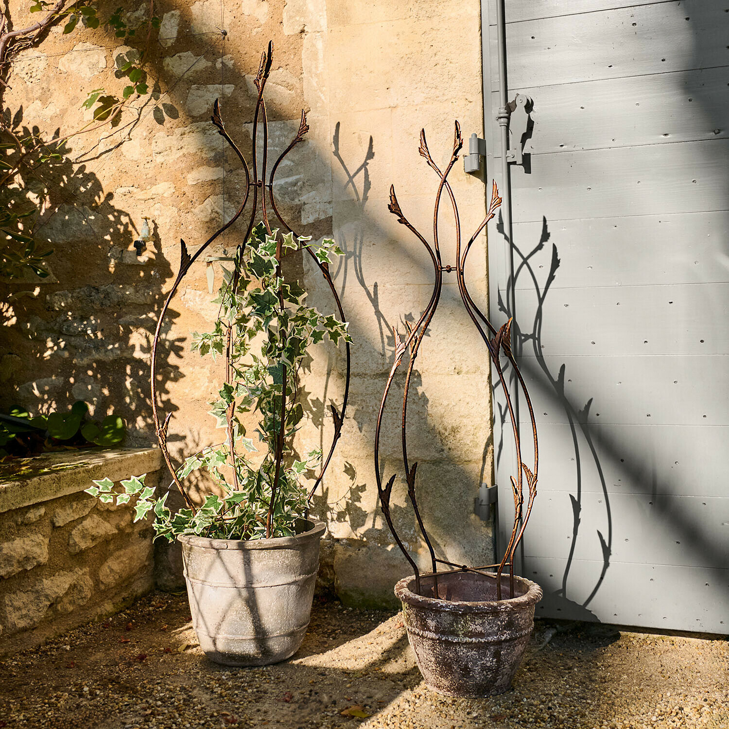 Dwa ozdobne metalowe rusztowania do roślin w donicach z kamienia na tarasie ogrodowym