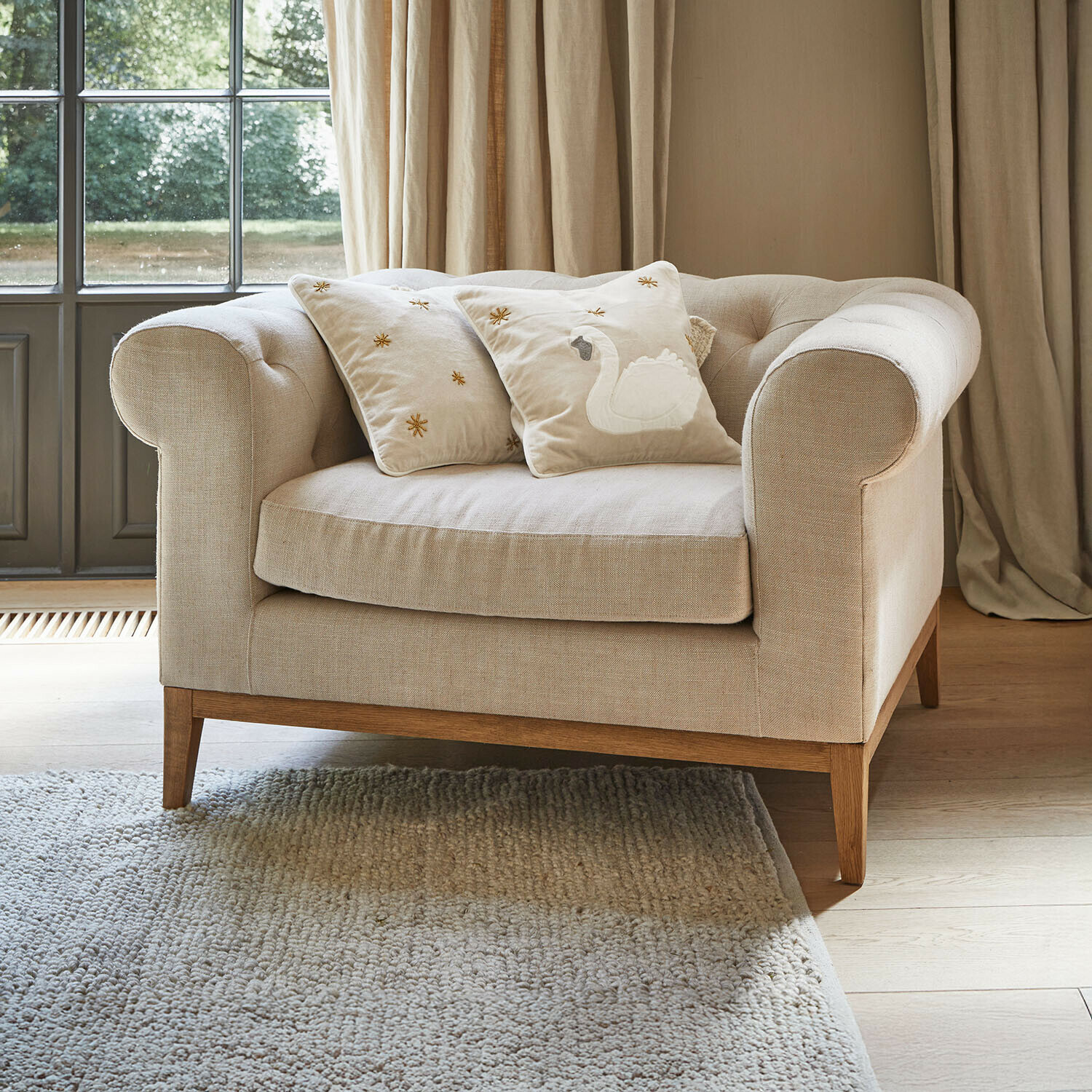 Fotel Fairbourne Beżowa sofa z tkaniny z drewnianą podstawą i dwoma ozdobnymi poduszkami z haftem łabędzia