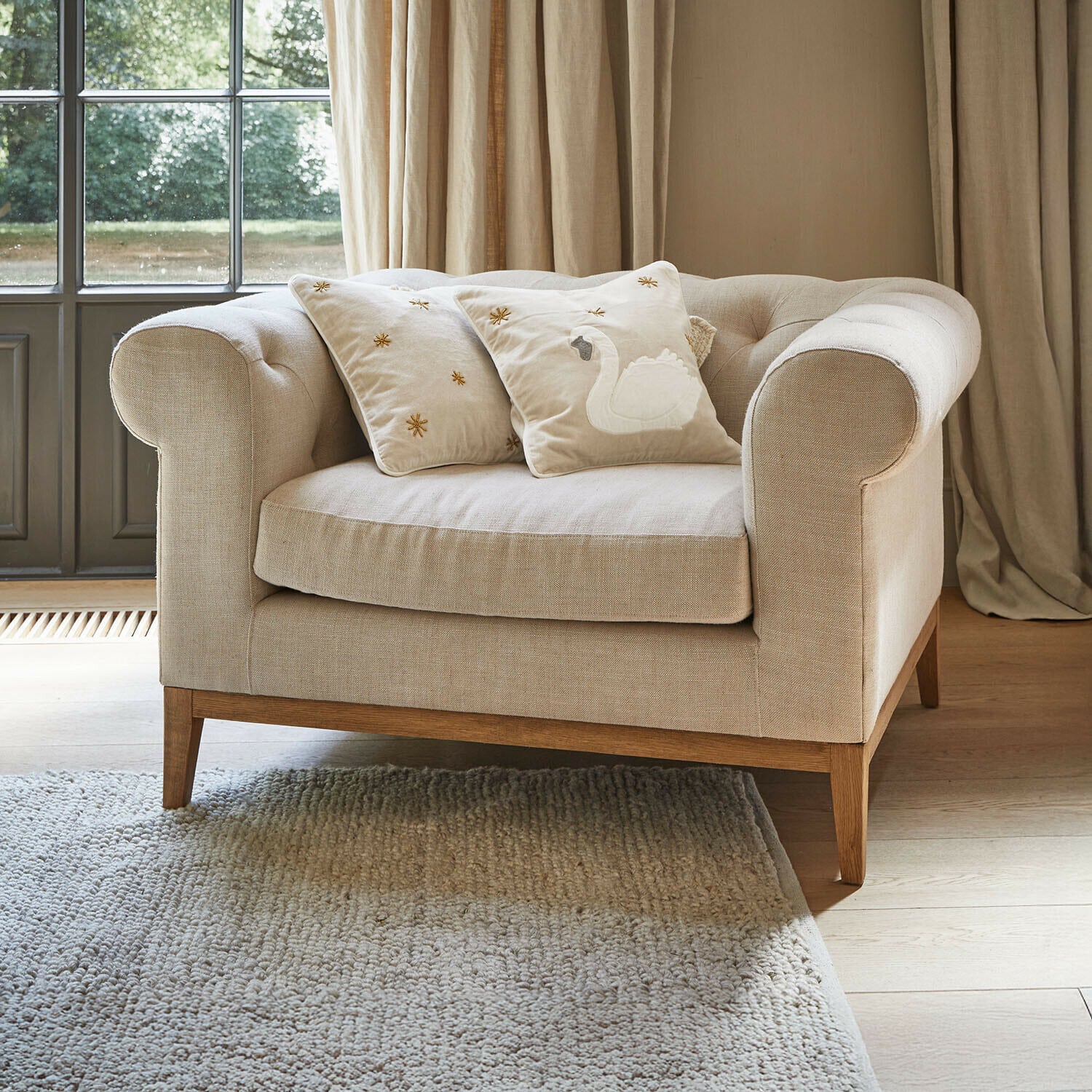 Fotel Fairbourne Beżowa sofa z tkaniny z drewnianą podstawą i dwoma ozdobnymi poduszkami z haftem łabędzia