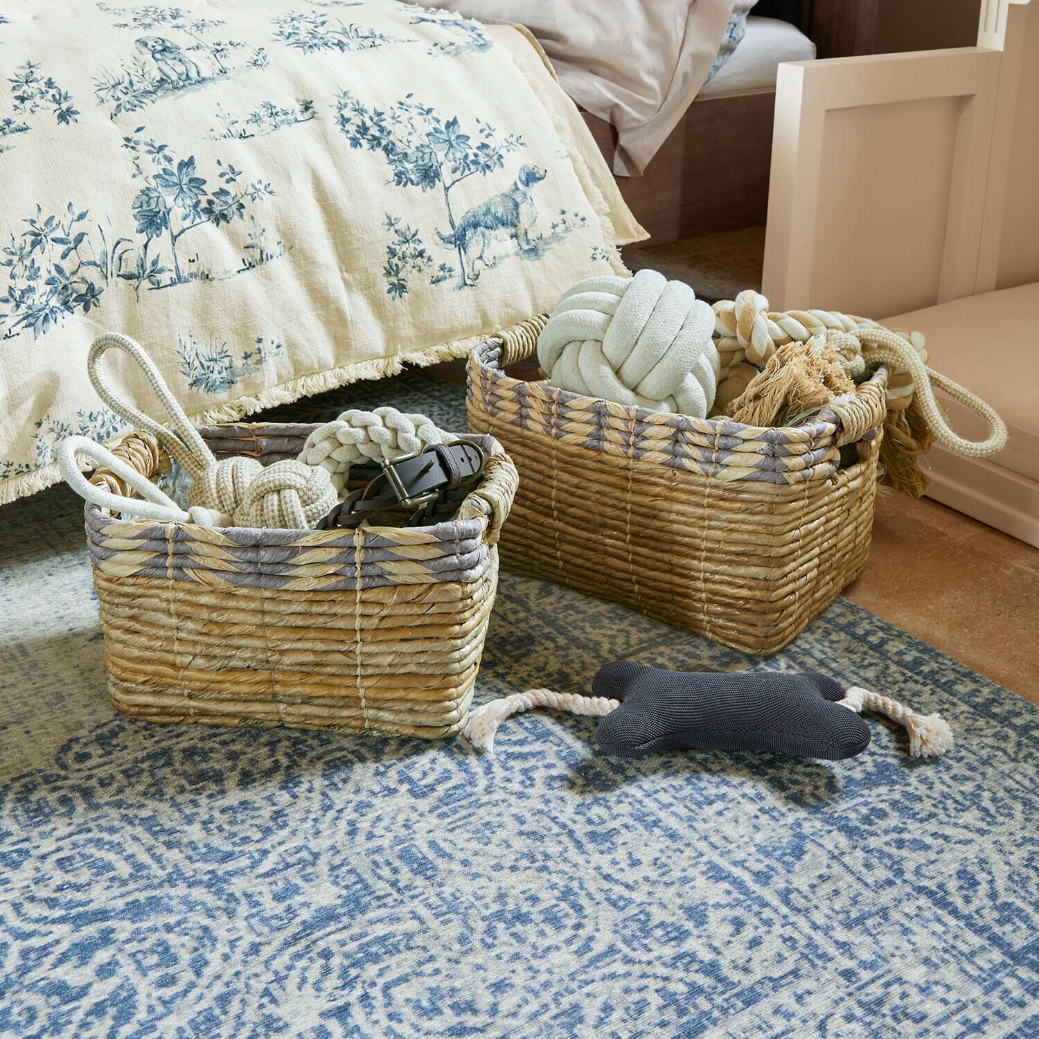 Dwa wiklinowe kosze z naturalnego materiału z zabawkami dla psów na niebieskim dywanie w sypialni