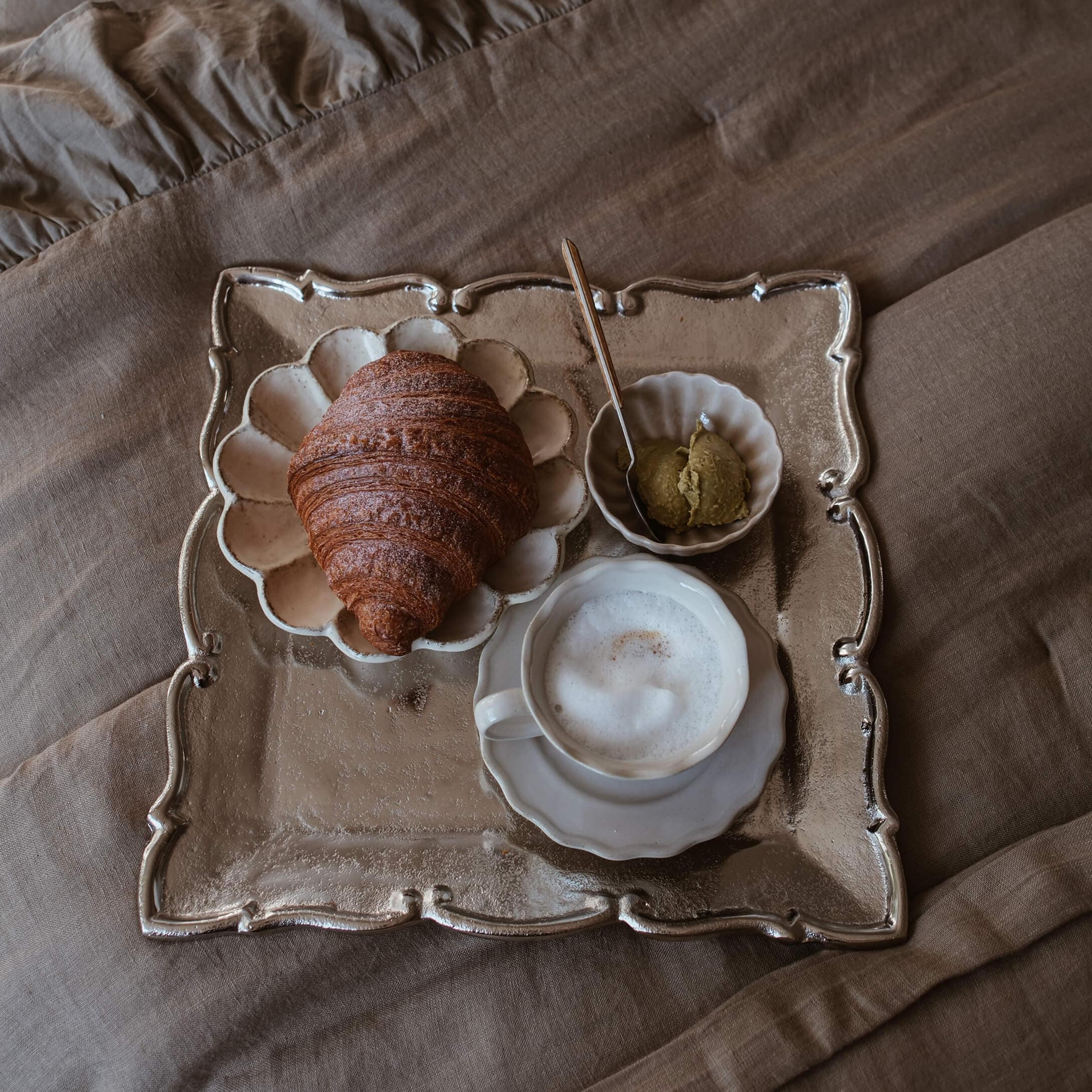 Taca z croissantem, kawą z pianką i pastą na beżowej tkaninie, styl slow living