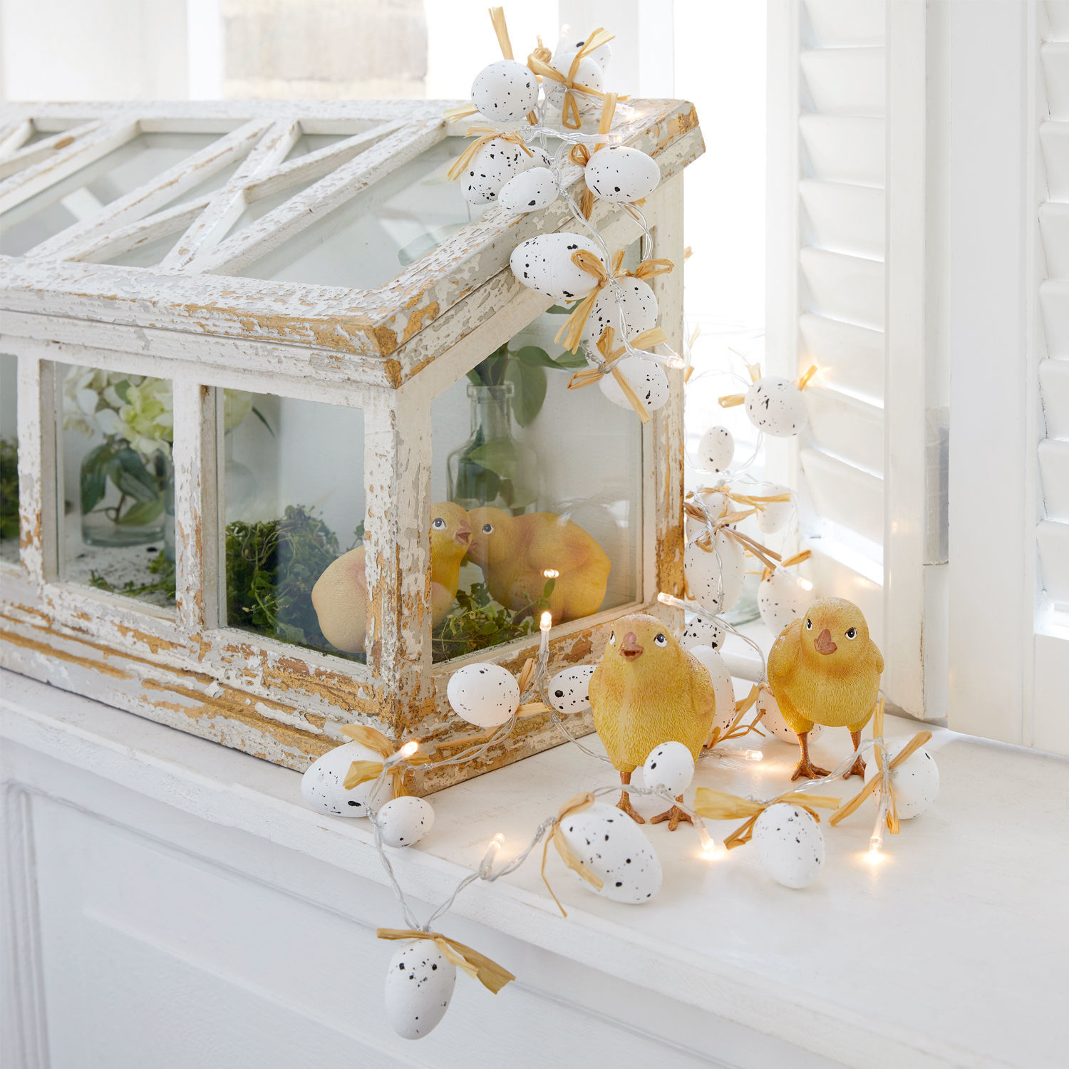 Dekoracyjna girlanda z białych jajek z kokardkami i żółtymi kurczakami na białym parapecie