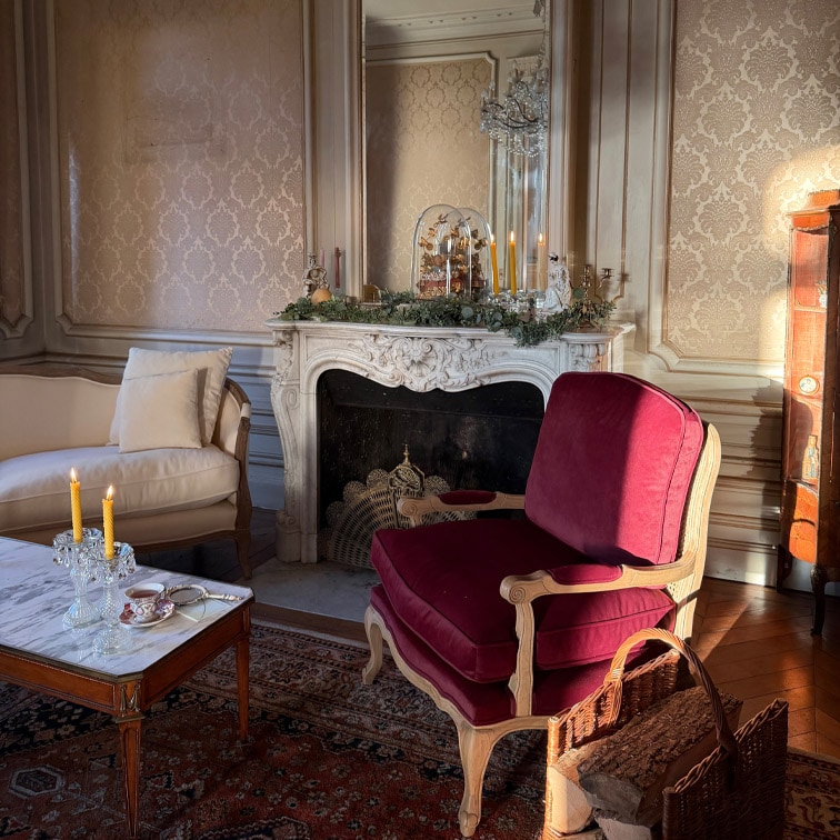 Klasyczny salon z bordowym fotelem z drewnianą ramą i marmurowym stolikiem z świecami