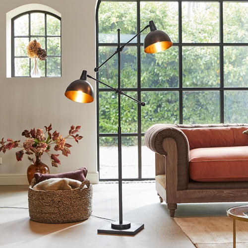 Czarna metalowa lampa podłogowa z dwoma regulowanymi kloszami w nowoczesnym salonie z pomarańczową sofą
