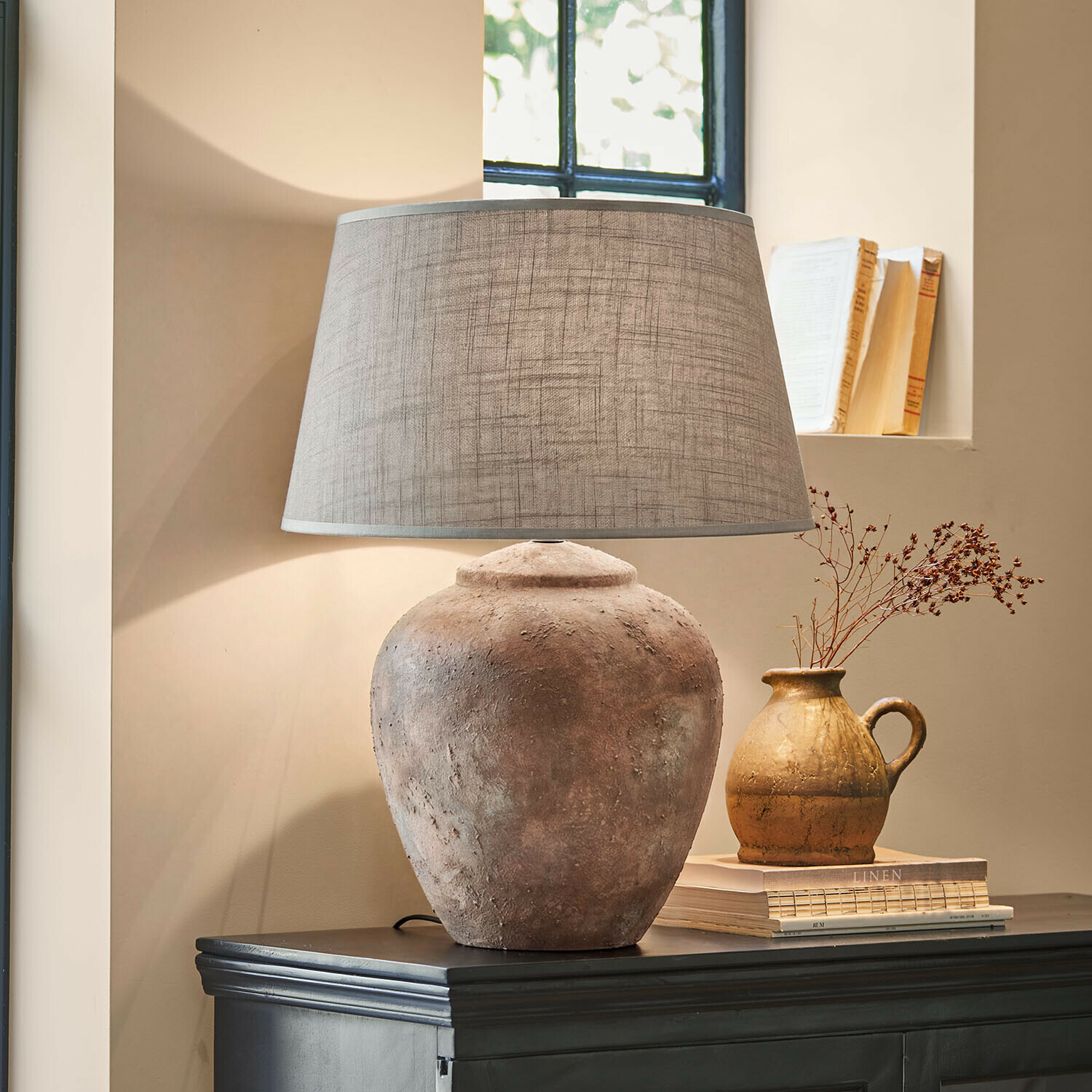 Lampa stołowa Kelvador Lampka stołowa z glinianą podstawą i szarym abażurem na ciemnej komodzie w przytulnym wnętrzu