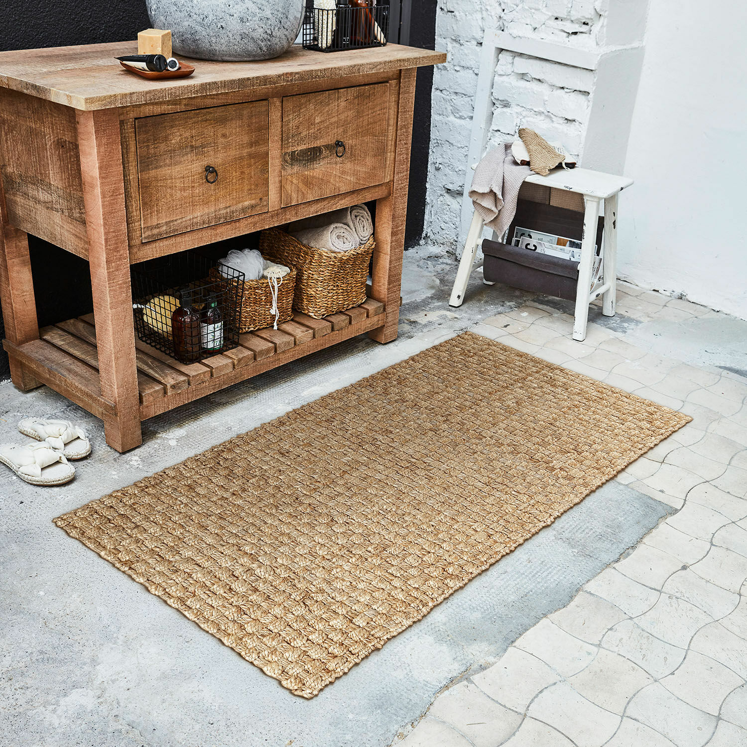 Chodnik Daoukro Dywanik z naturalnego juty w kolorze beżowym na podłodze obok drewnianej szafki i białego stołka