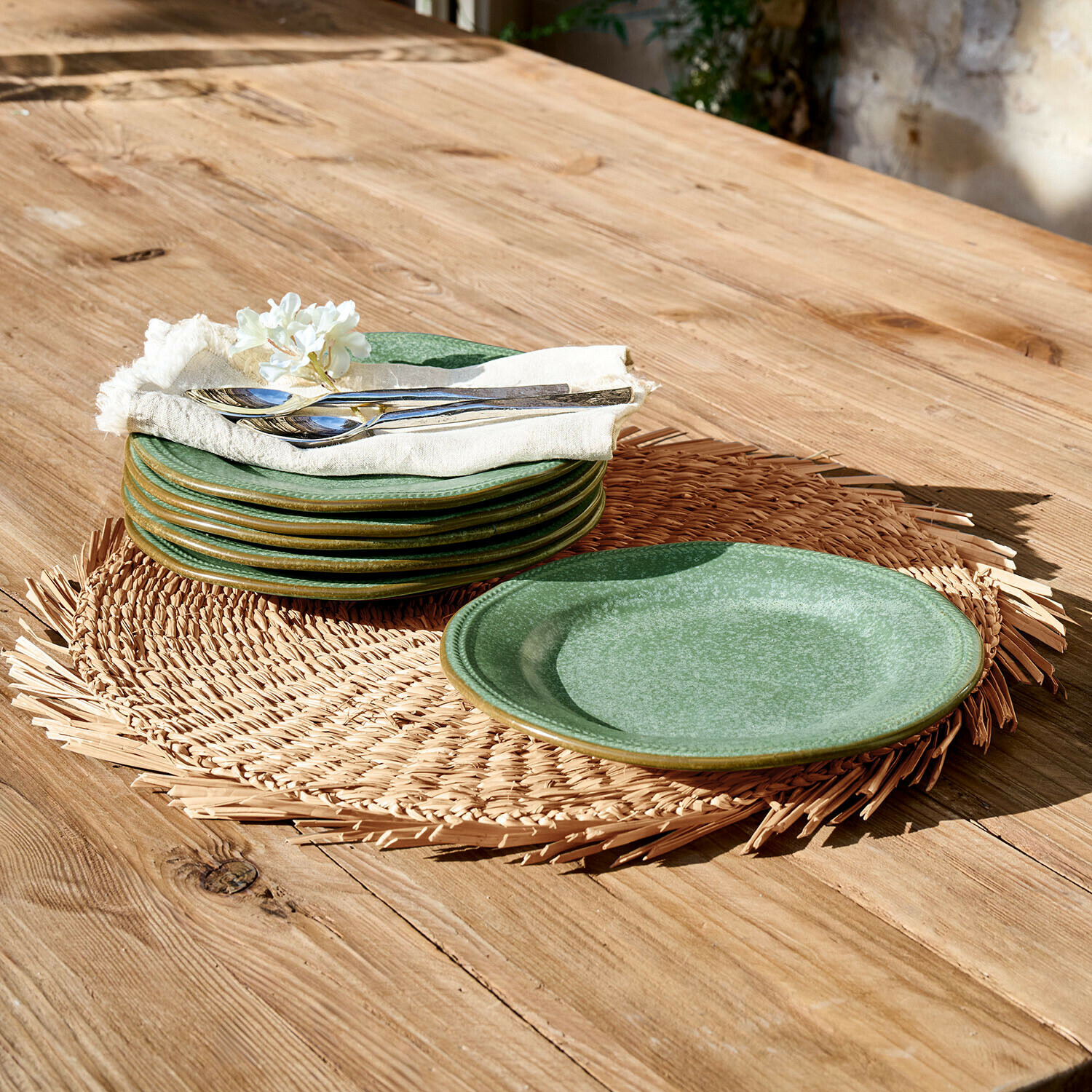 Zestaw zielonych ceramicznych talerzy na plecionym podkładce na drewnianym stole z metalowymi sztućcami
