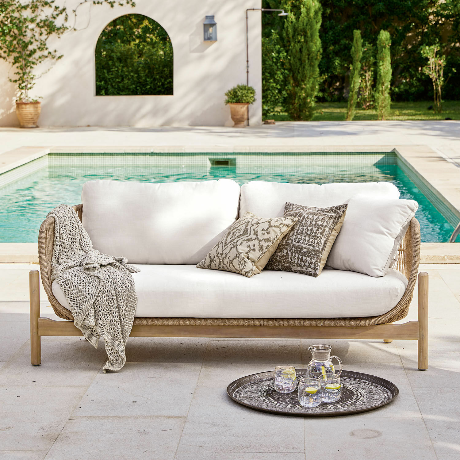 Sofa FSC®-100% Sofa ogrodowe z jasnymi poduszkami i drewnianą ramą przy basenie, dekoracyjne poduszki i koc