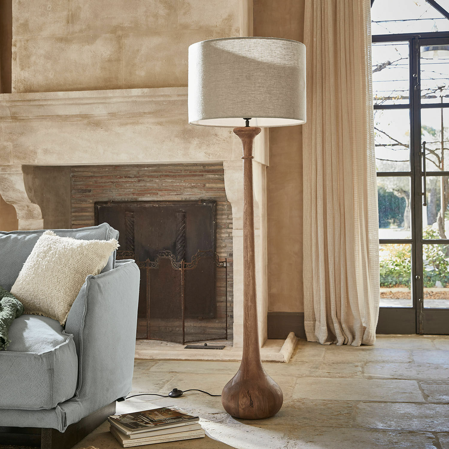 Lampa stojąca Andrées Lampa podłogowa z drewnianą podstawą i beżowym abażurem w przytulnym salonie z kominkiem