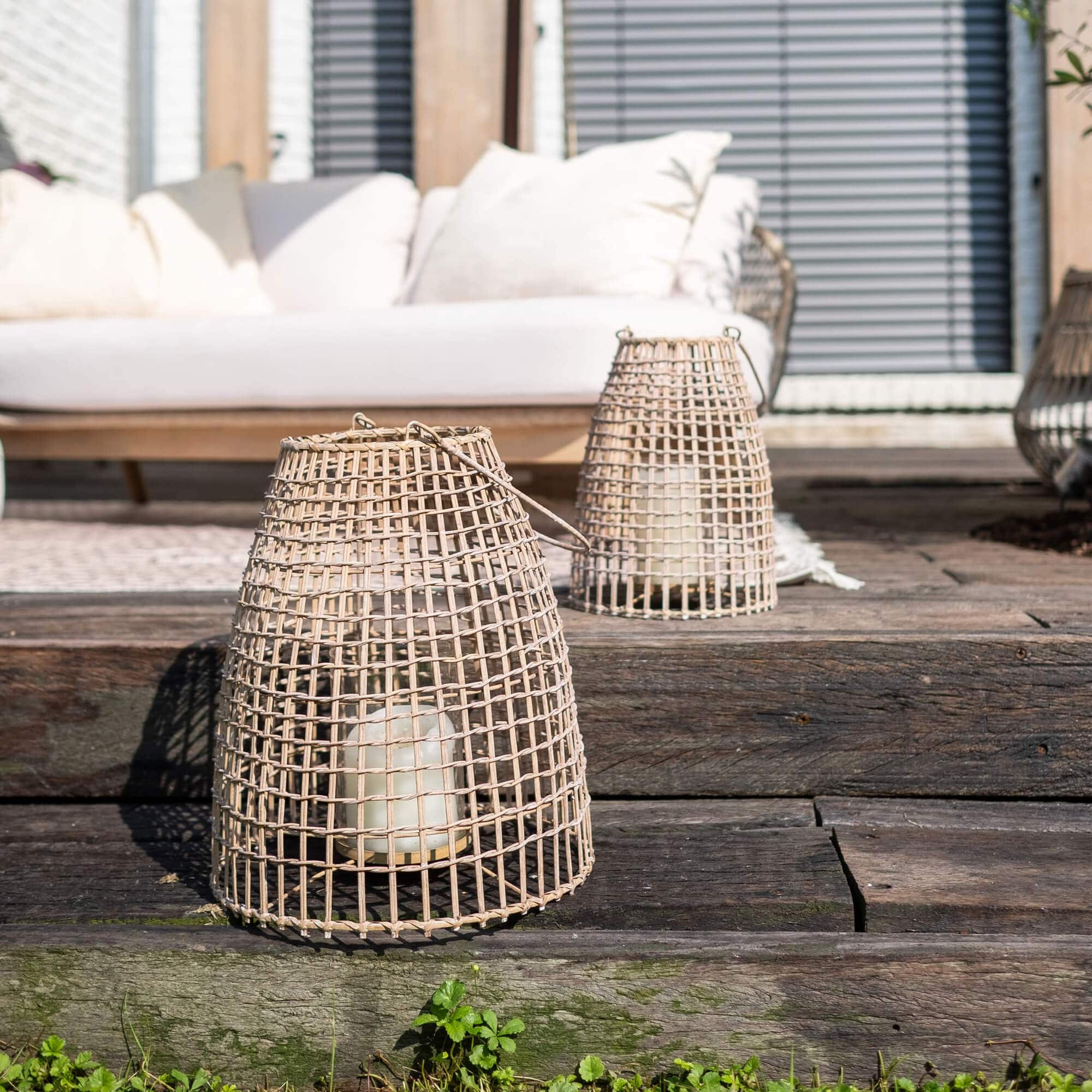 Lampion z wikliny w naturalnym kolorze z białą świecą na drewnianym tarasie