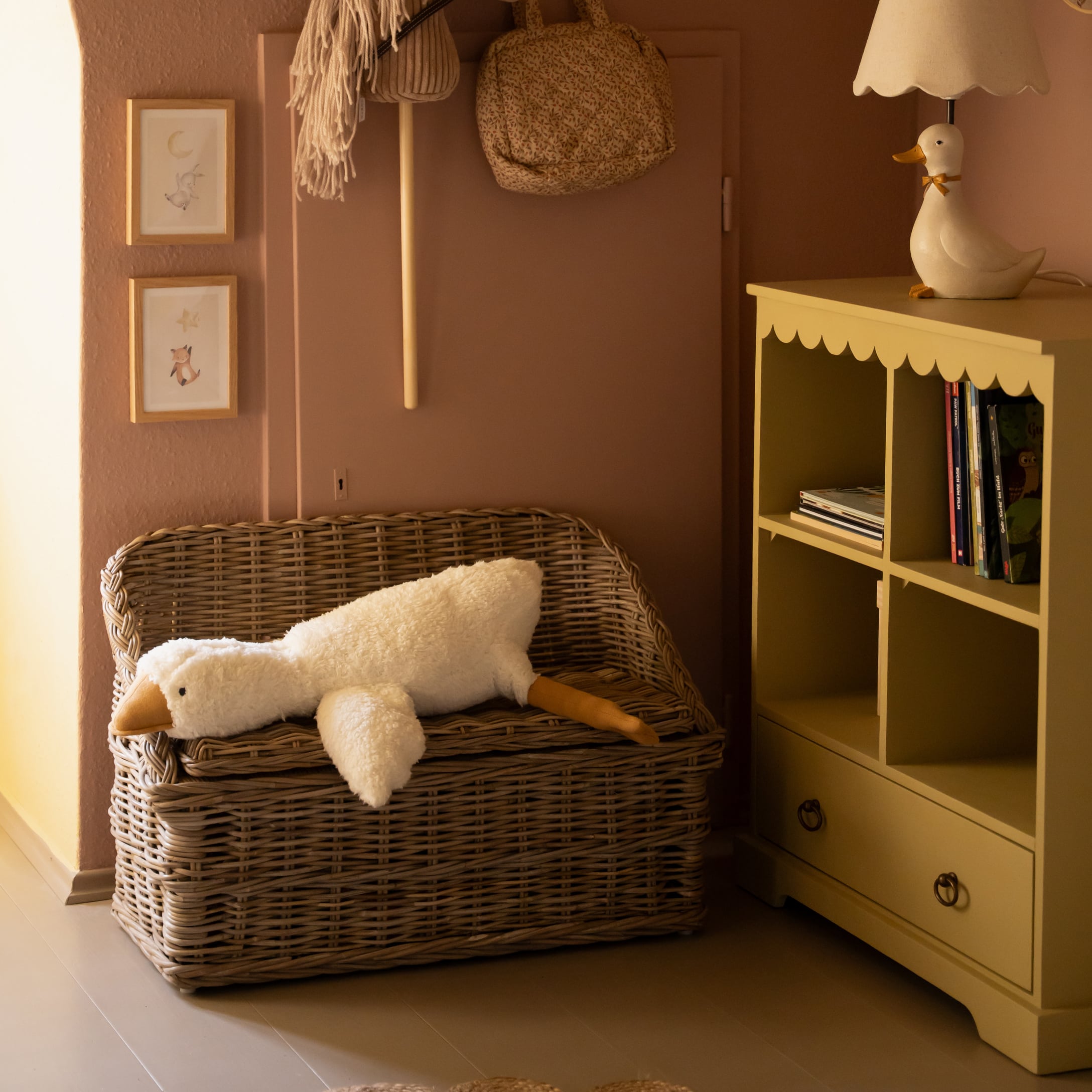 Wiklinowa ławka z miękkim białym pluszowym podłużnym pluszakiem kaczki w przytulnym pokoju dziecięcym