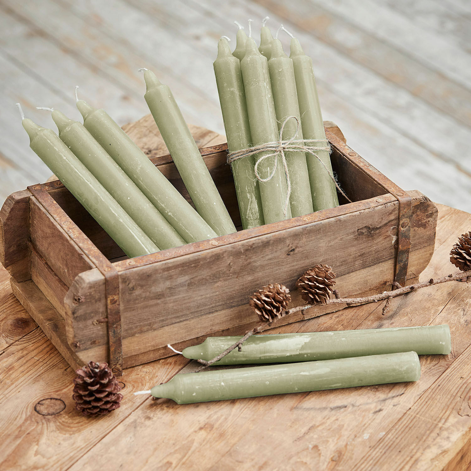 Świeca, zestaw 12 szt. Bauceau Zestaw zielonych świec stołowych z wosku w drewnianym pudełku na rustykalnym stole z szyszkami
