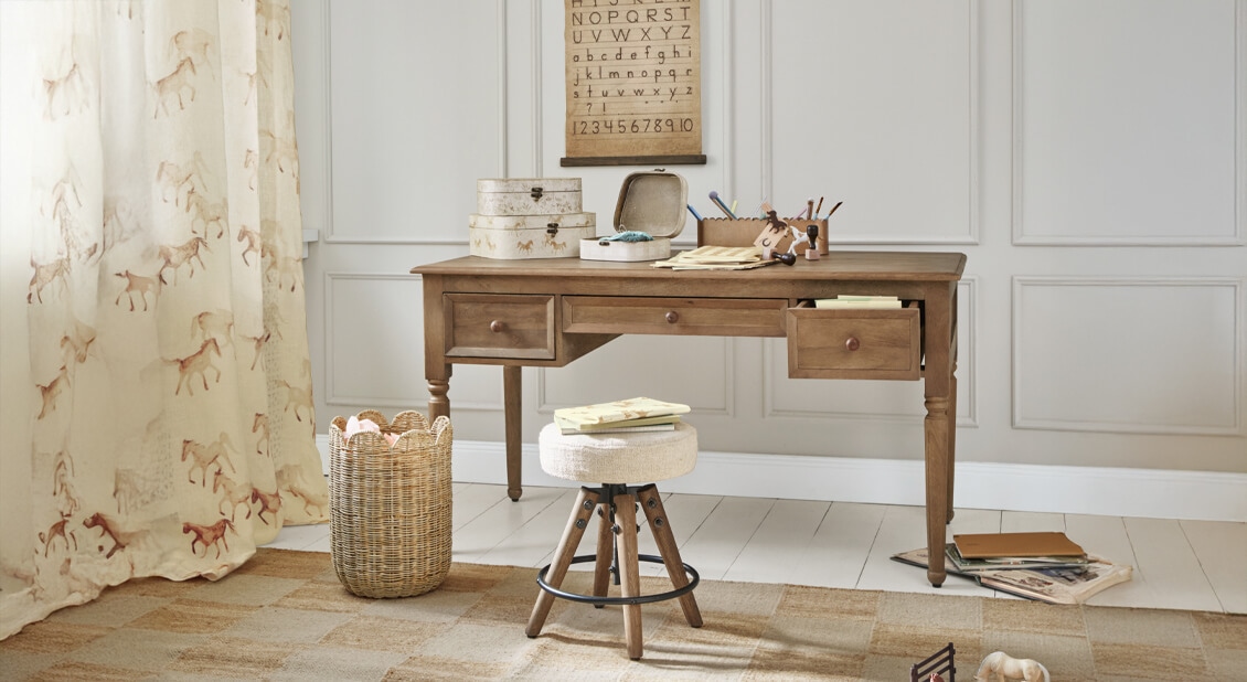 Drewniane biurko z trzema szufladami i stołek z jasnym obiciem w przytulnym pokoju do nauki