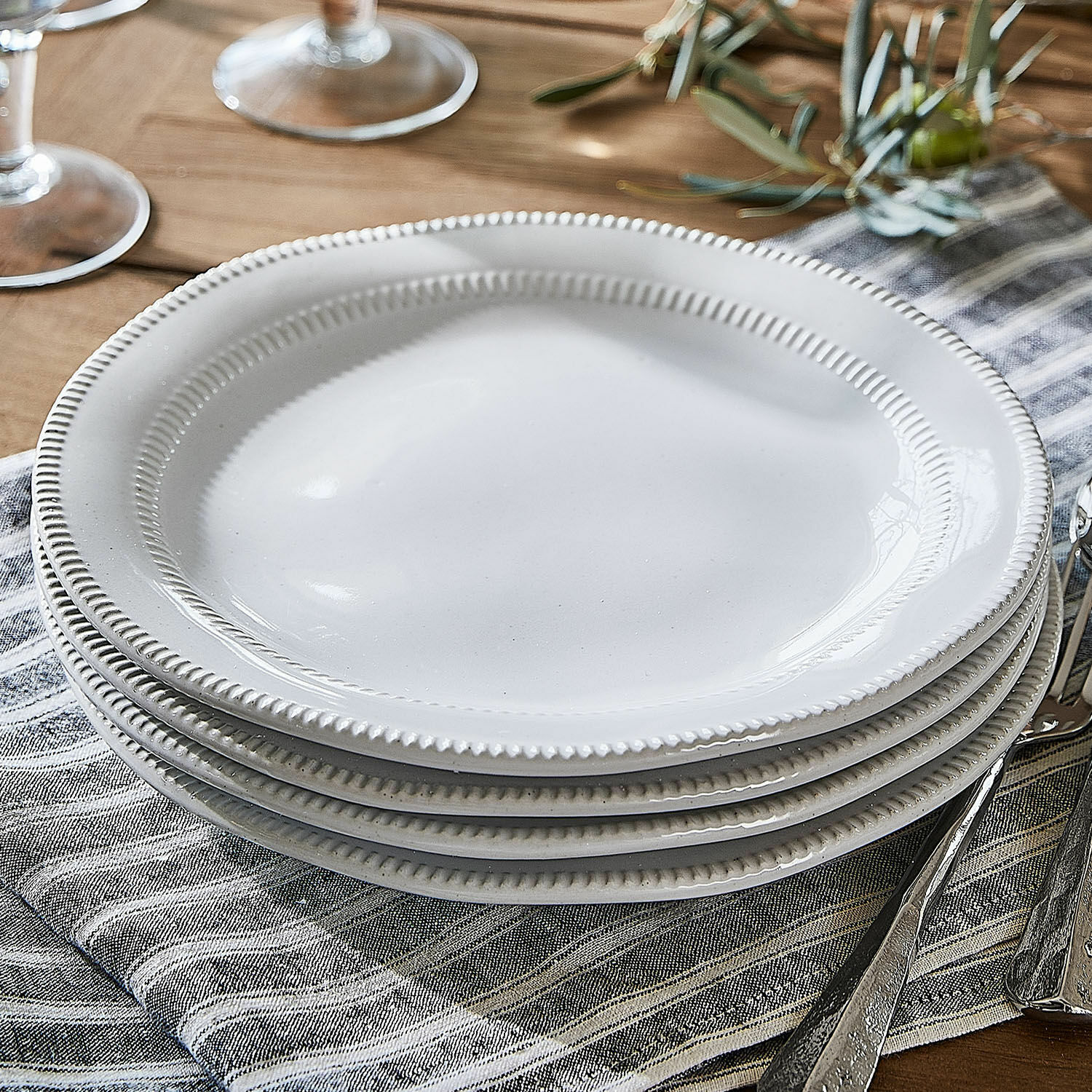 Małe talerze Alentejo Białe ceramiczne talerze z ozdobnym brzegiem na lnianej serwetce na drewnianym stole