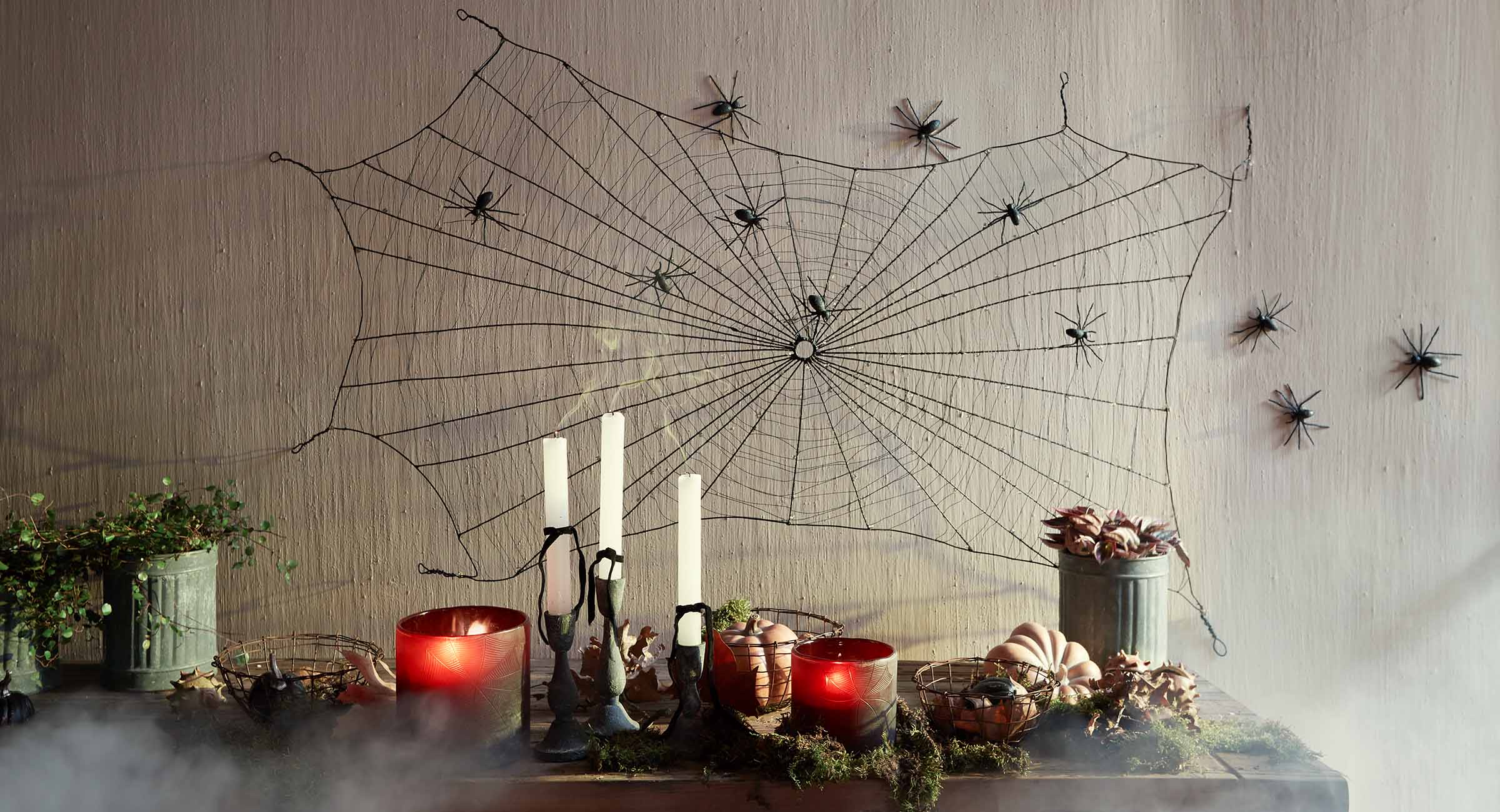 Dekoracja Halloween z czarną pajęczyną i pająkami na ścianie oraz świecami i dyniami na stole