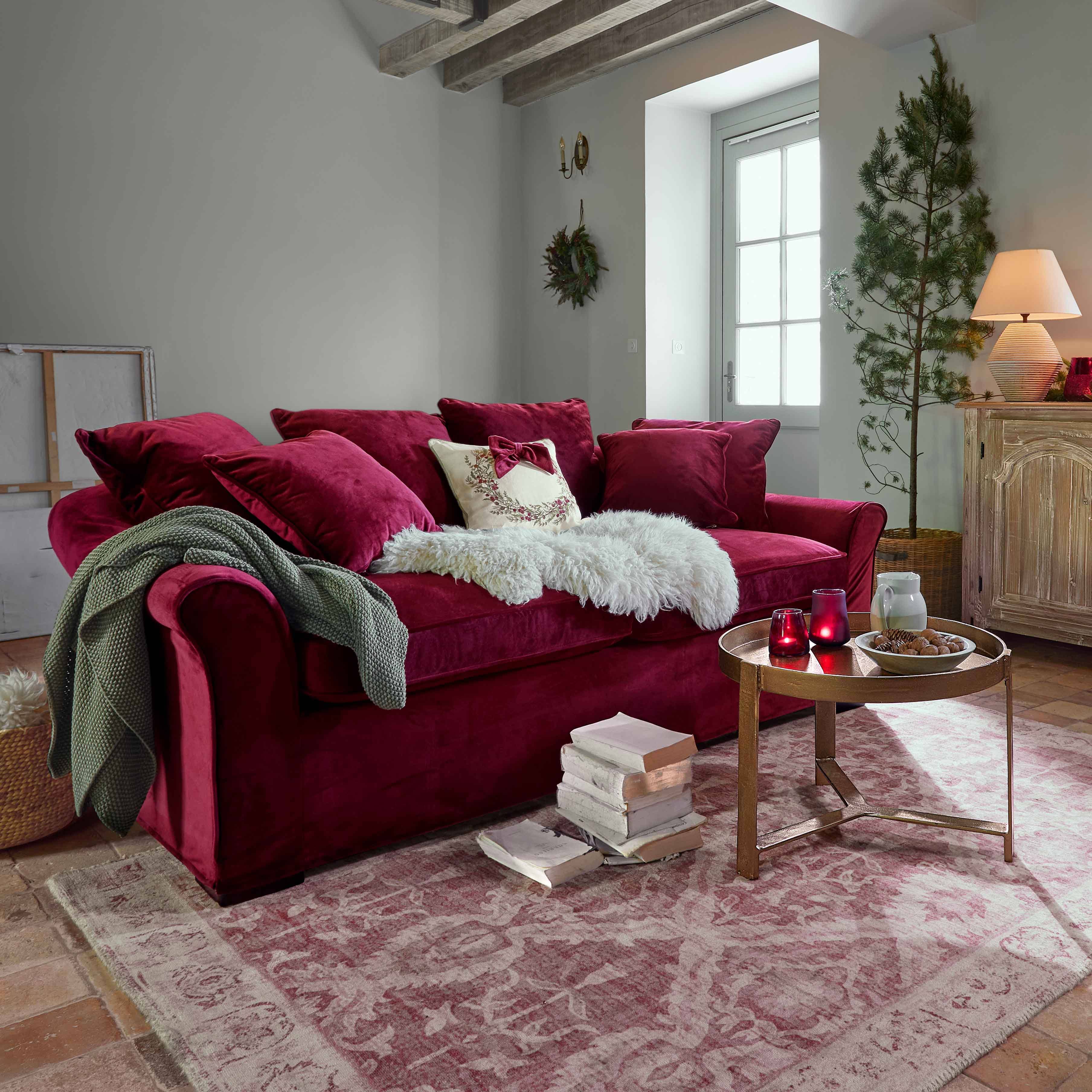 Bordowa welurowa sofa z poduszkami i miękkim kocem w przytulnym salonie z drewnianymi belkami