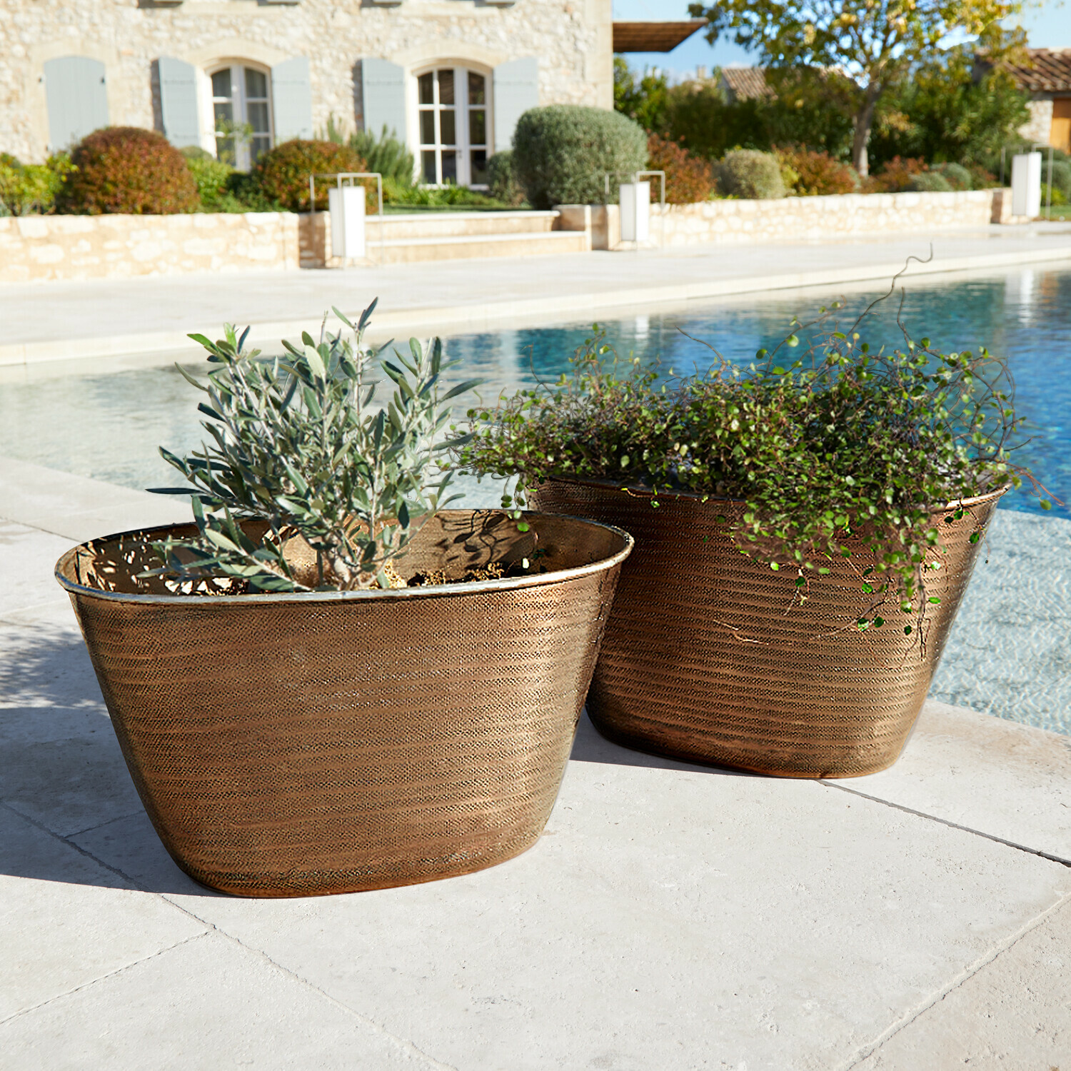 Dwa miedziane donice z roślinami obok basenu na tarasie z kamienia, dekoracja ogrodowa