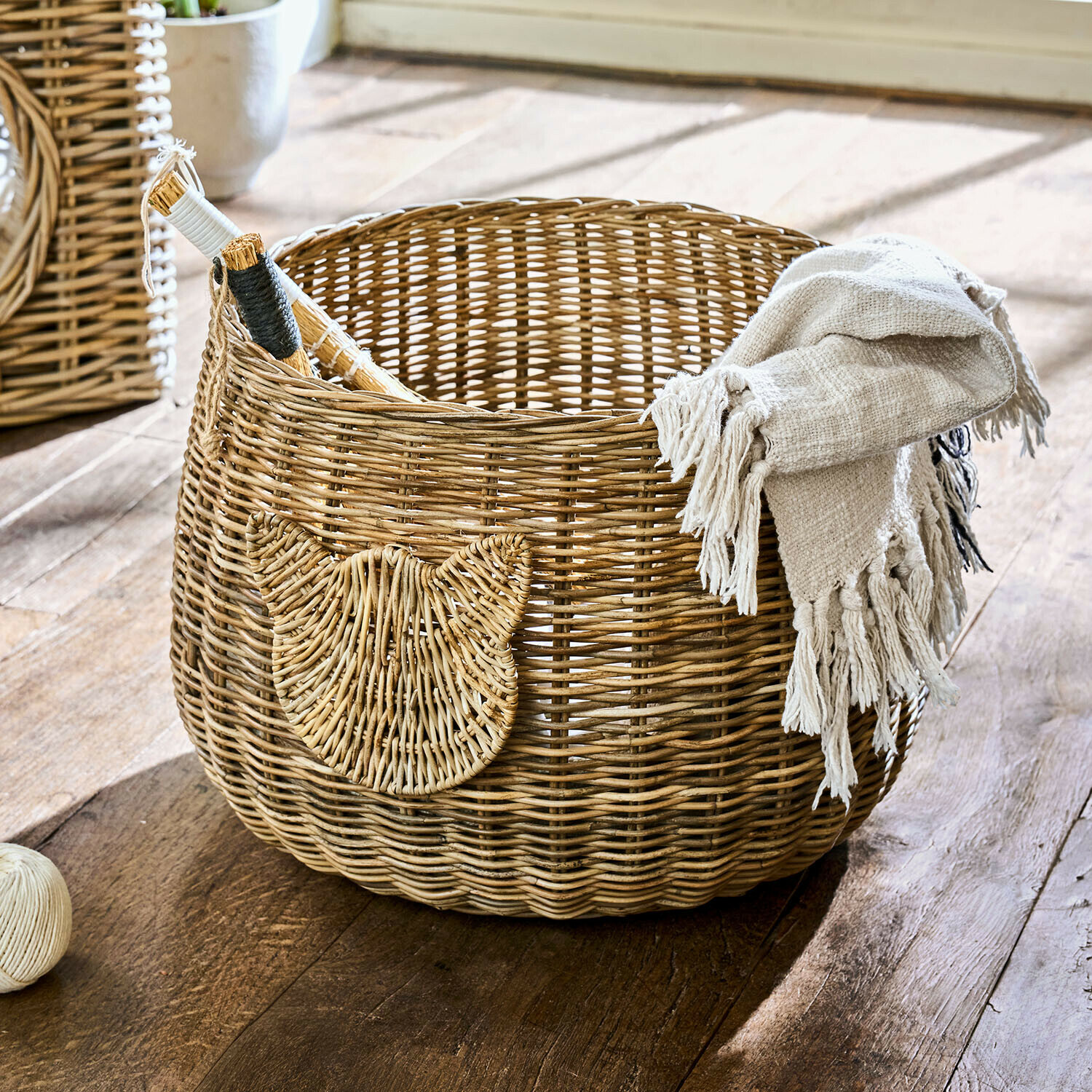 Okrągły kosz z rattanu w naturalnym kolorze z ozdobą w kształcie kota i beżowym kocem