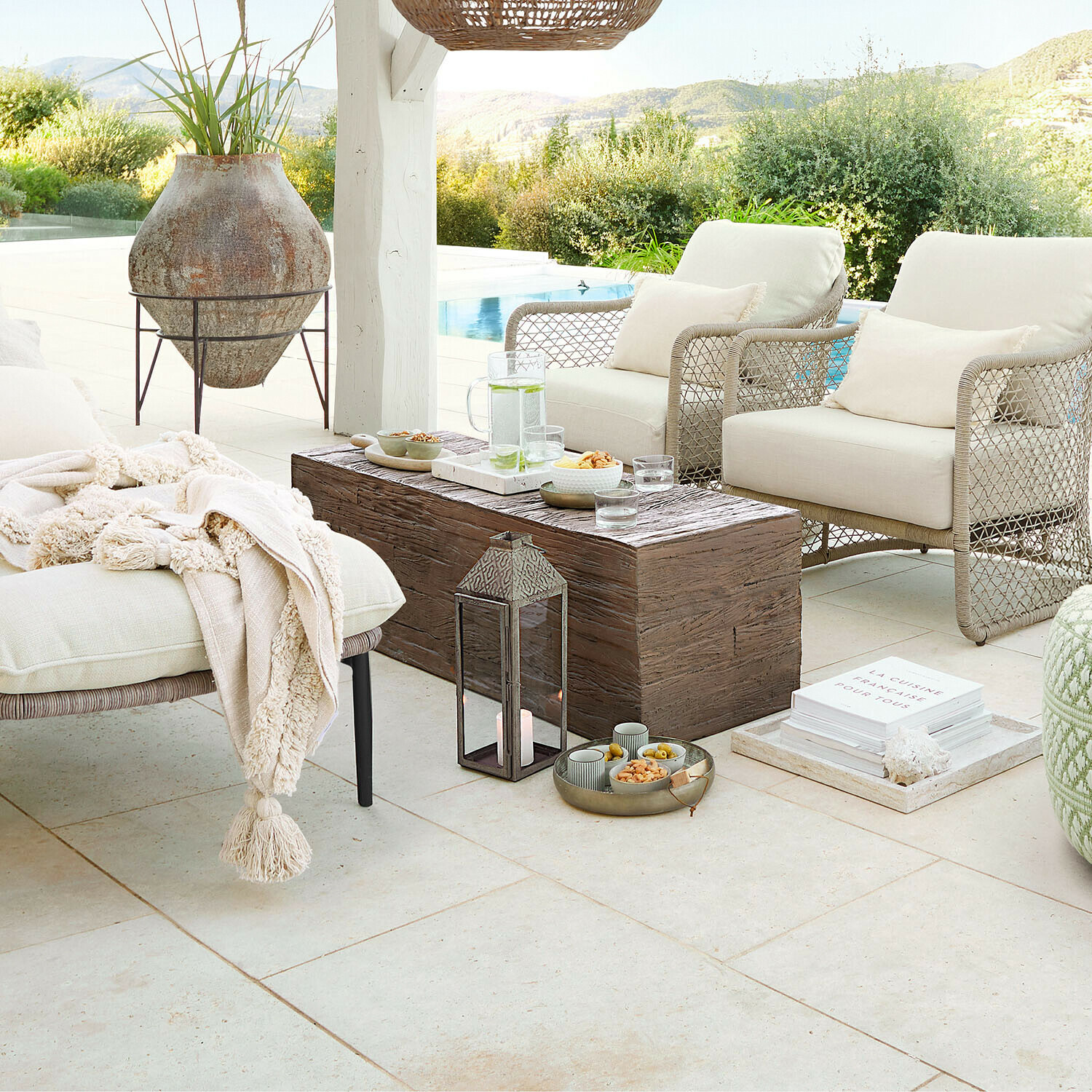 Przytulny zestaw mebli ogrodowych z beżowymi poduszkami i drewnianym stolikiem na tarasie z widokiem na basen